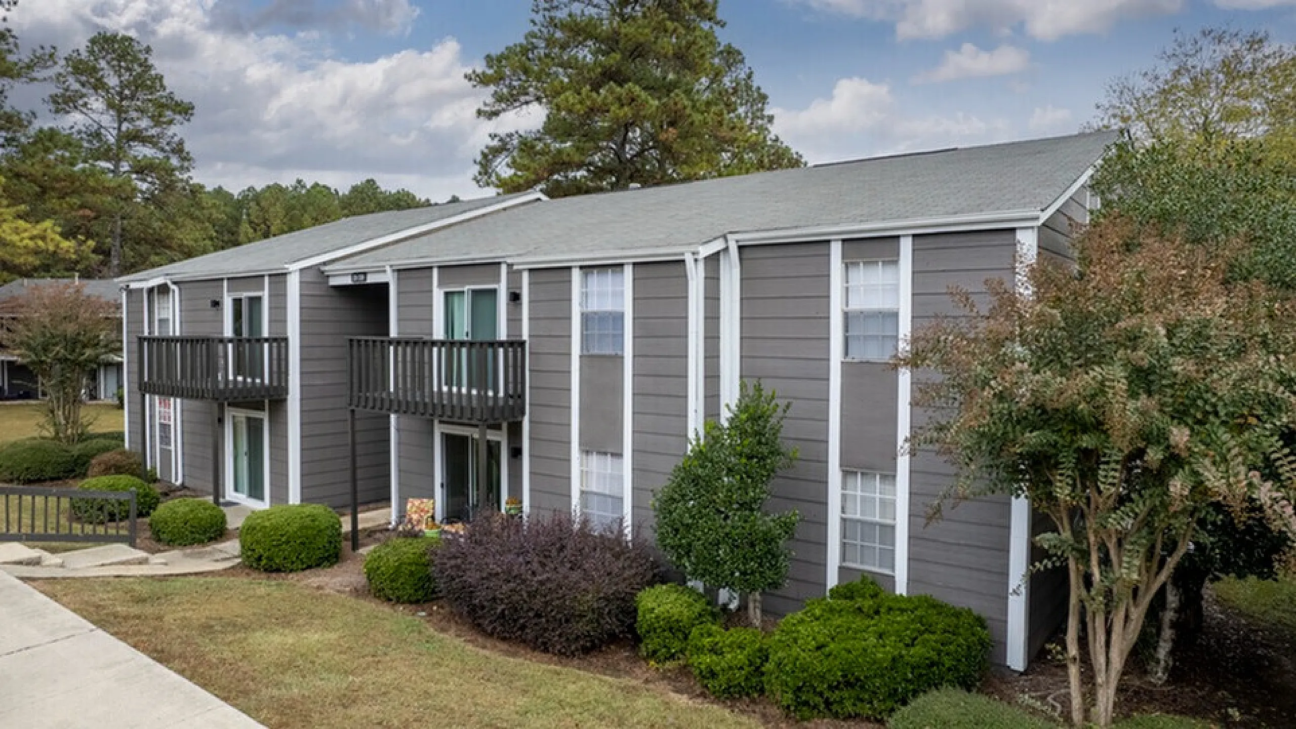 Charming apartment building with classic exterior, surrounded by lush greenery and peaceful trees, offering serene living.