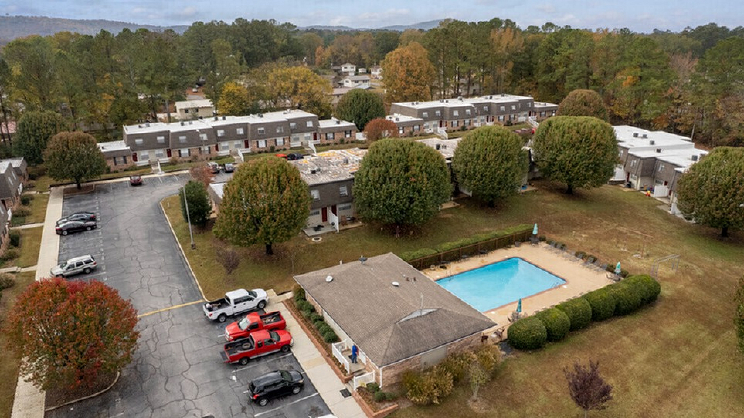 Charming aerial view of a serene residential community featuring a sparkling swimming pool, lush greenery, and neatly arranged townhomes perfect for family living.