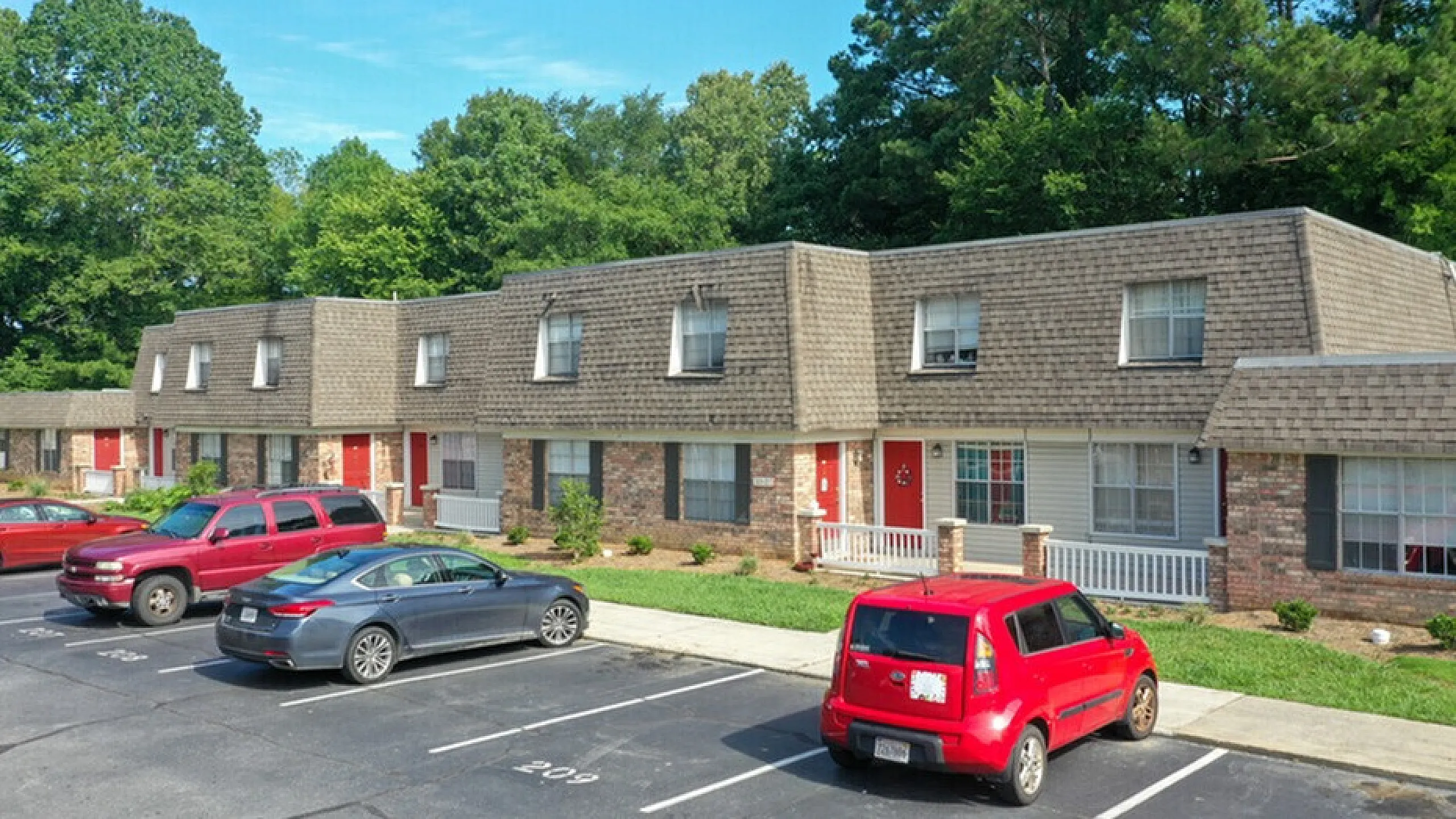 Inviting townhouse complex with cozy front porches and ample parking surrounded by lush greenery.