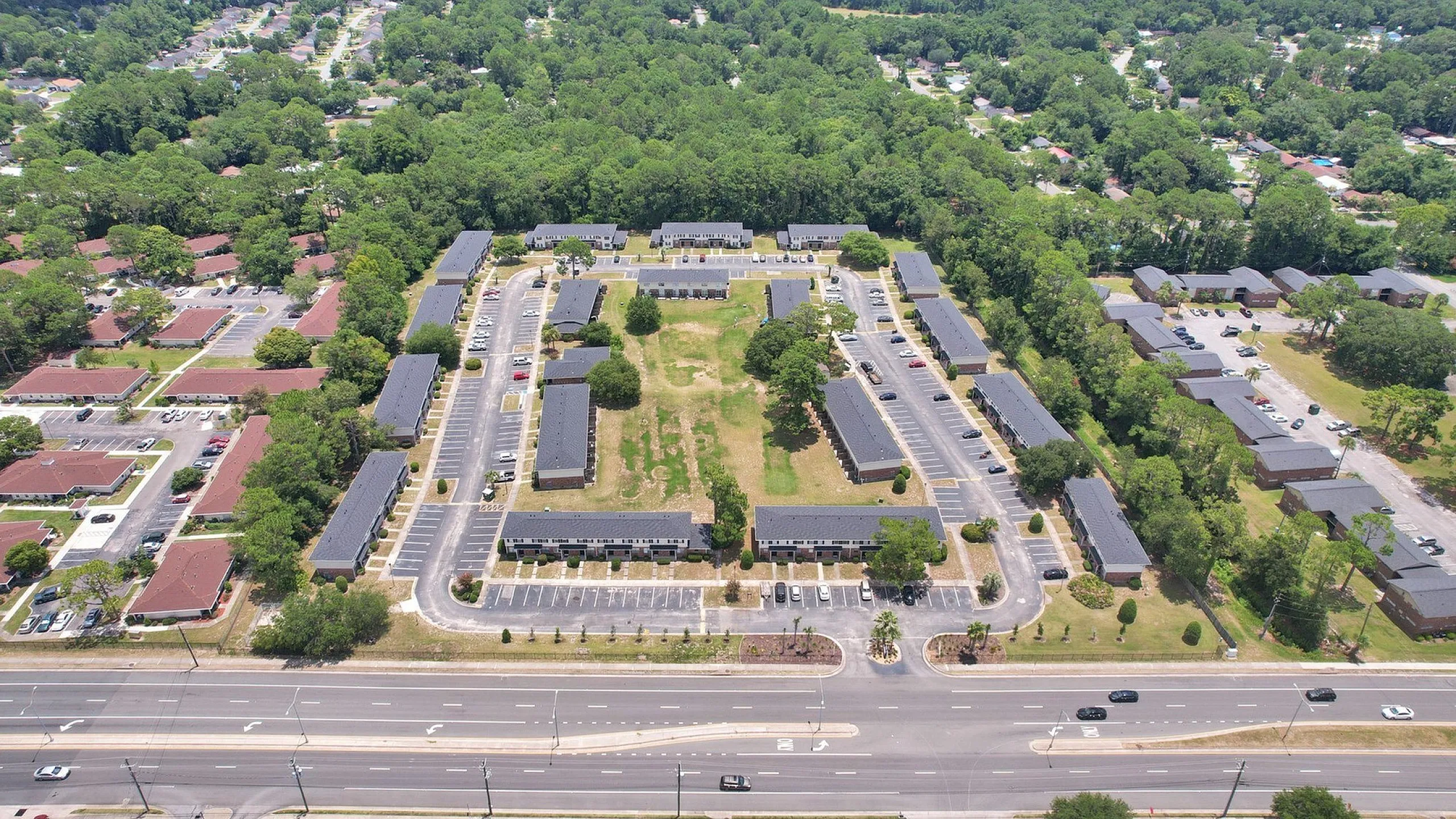 Expansive aerial view of a modern apartment complex featuring multiple buildings surrounded by lush greenery and ample parking, offering a serene suburban atmosphere.