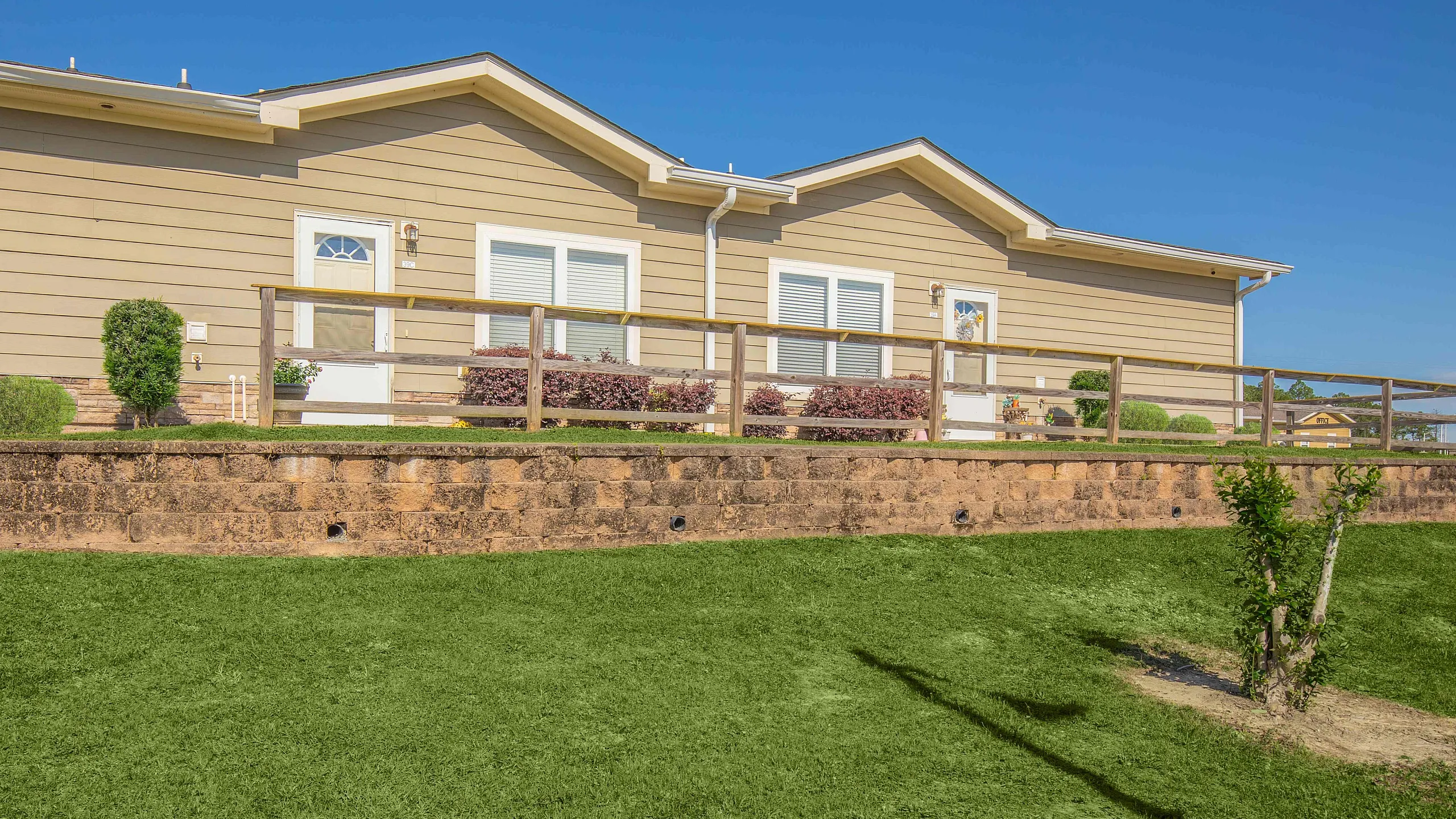 Charming dual-unit townhouse with lush front lawn and rustic wooden fencing, basking in bright sunlight.