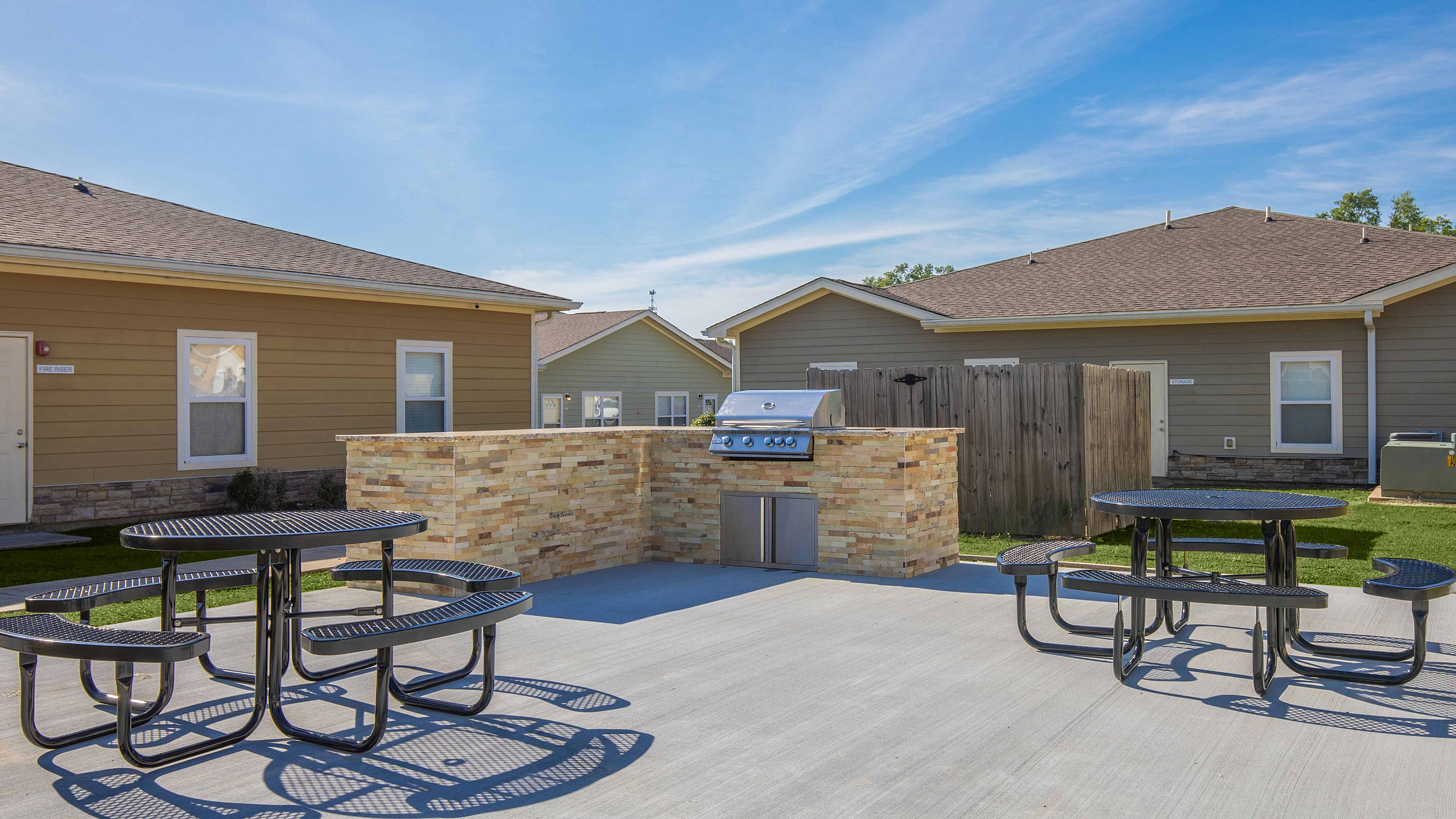 Charming outdoor area featuring stone grilling station, picnic tables, and modern patio space, perfect for social gatherings.