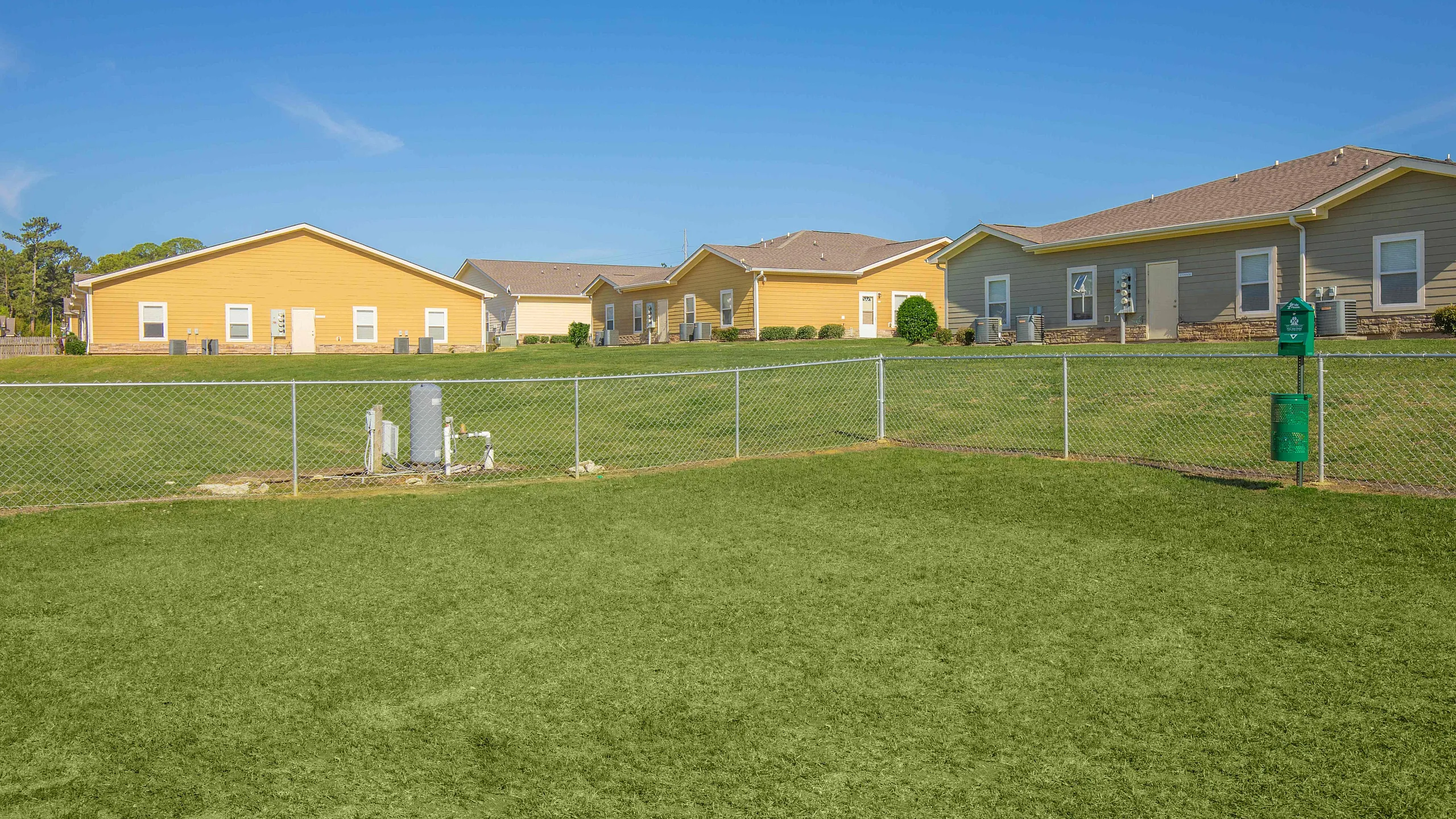Charming single-story homes with a spacious green yard, fenced for privacy, under a clear blue sky.
