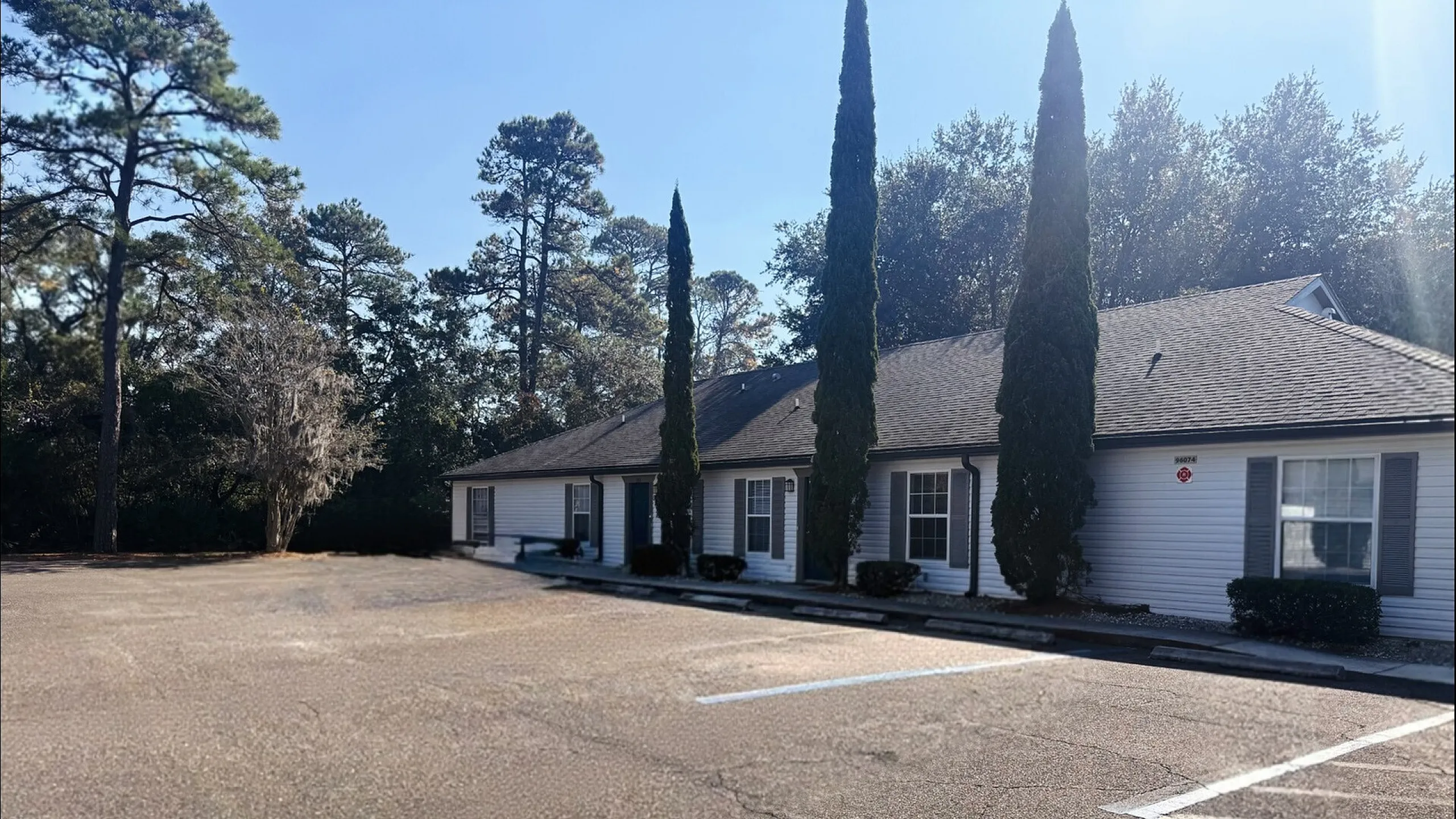 Inviting exterior of a modern apartment building surrounded by tall trees, featuring ample parking space and elegant architectural design.