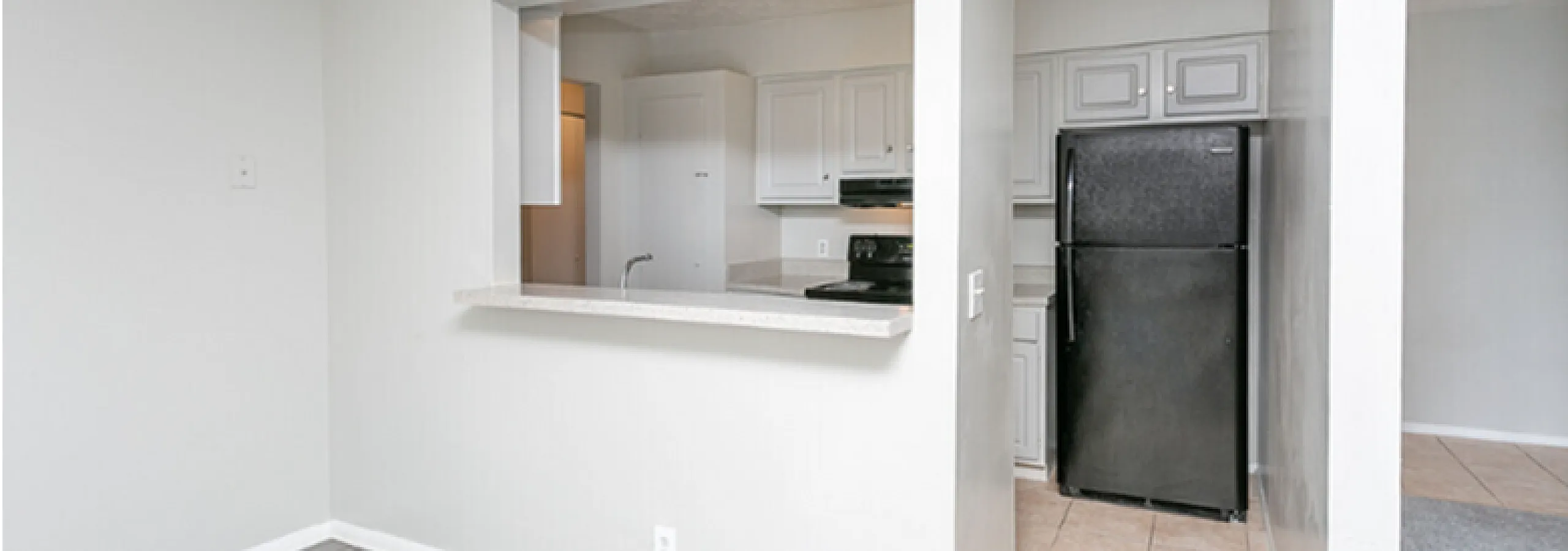 Contemporary apartment kitchen with sleek black appliances, open serving hatch, and stylish tile flooring.