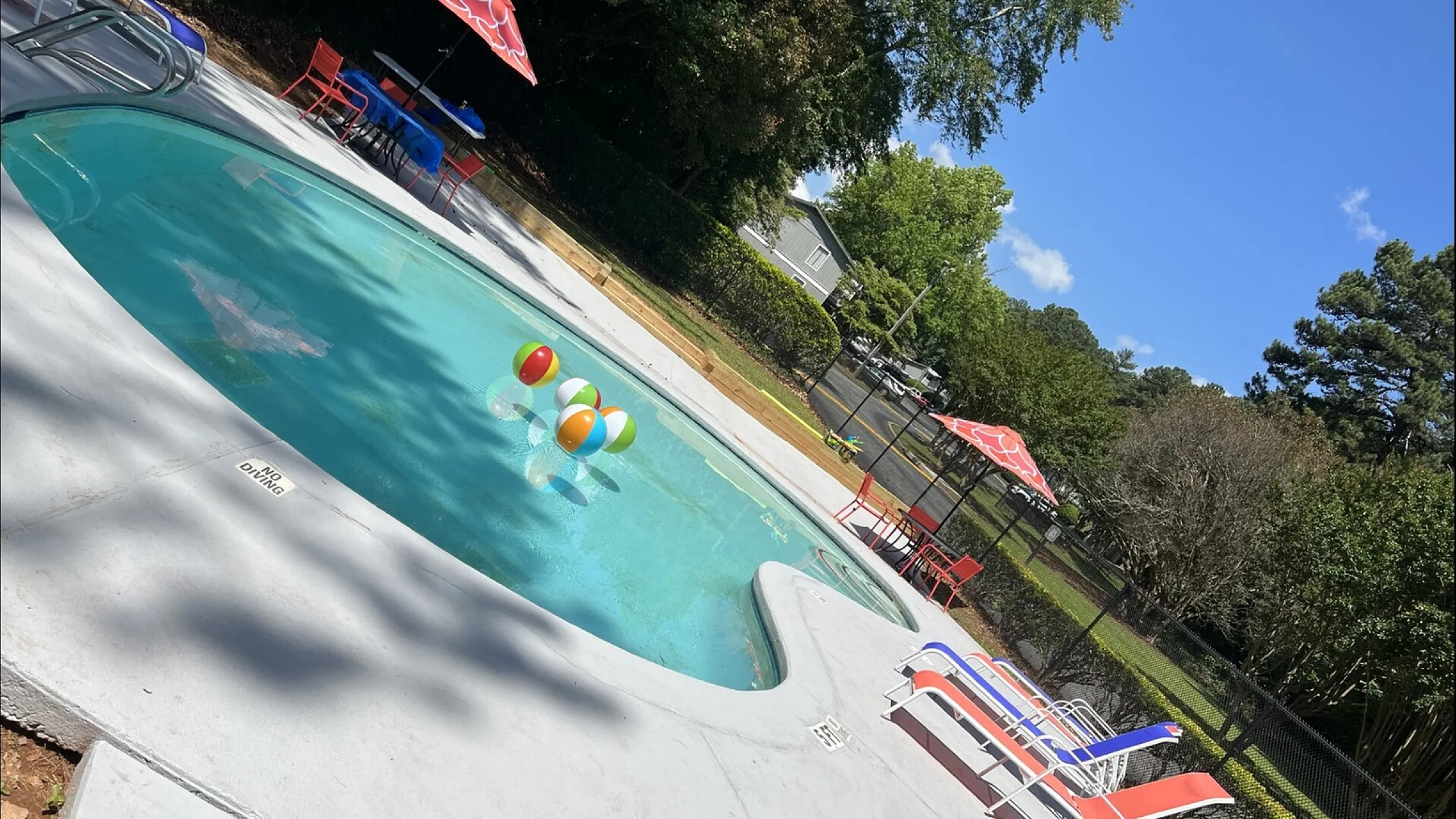 Inviting outdoor pool with vibrant beach balls and colorful lounge chairs, set against a backdrop of lush greenery and a clear blue sky.