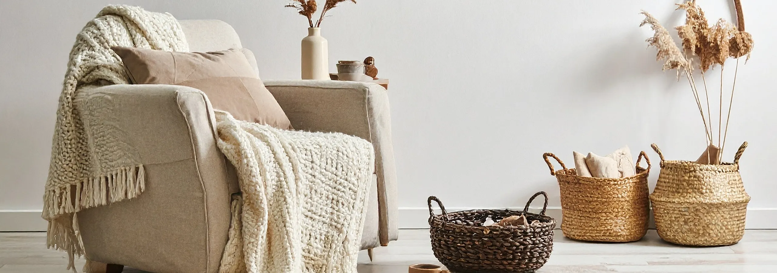 Cozy living room corner featuring a plush armchair draped with a knit throw, surrounded by chic woven baskets and elegant dried decor.