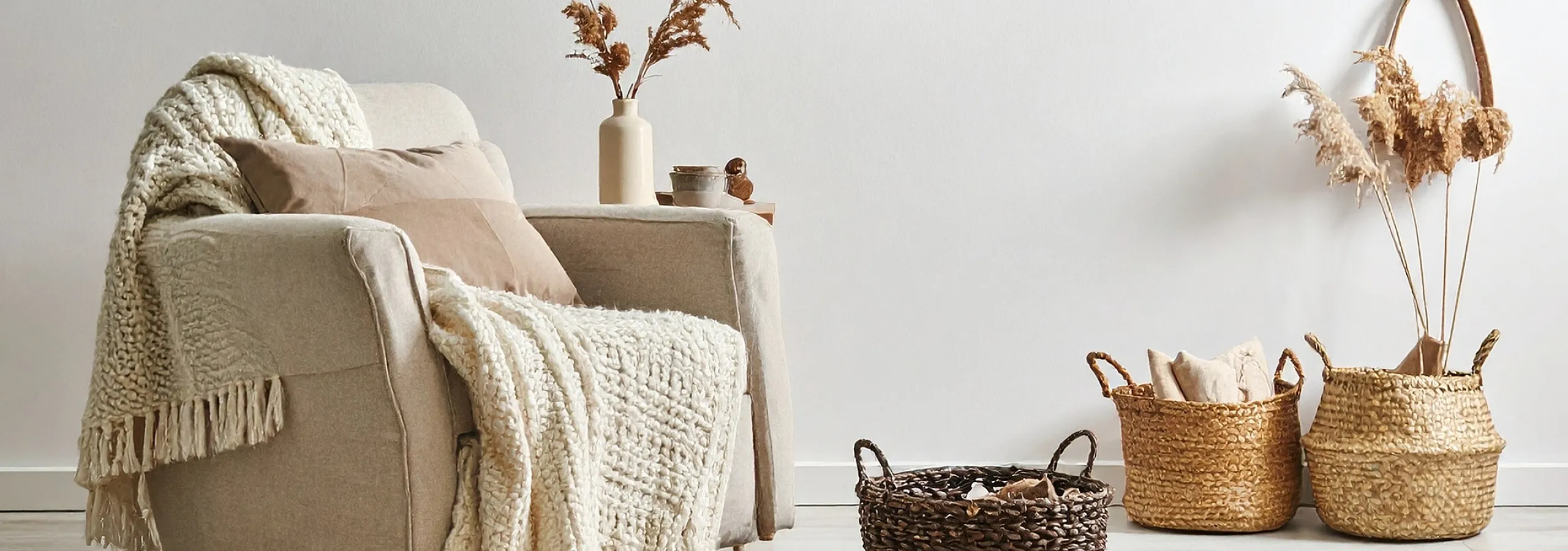Cozy living room corner with a plush armchair draped in a textured throw, surrounded by elegant woven baskets and artistic decor, exuding warmth and style.