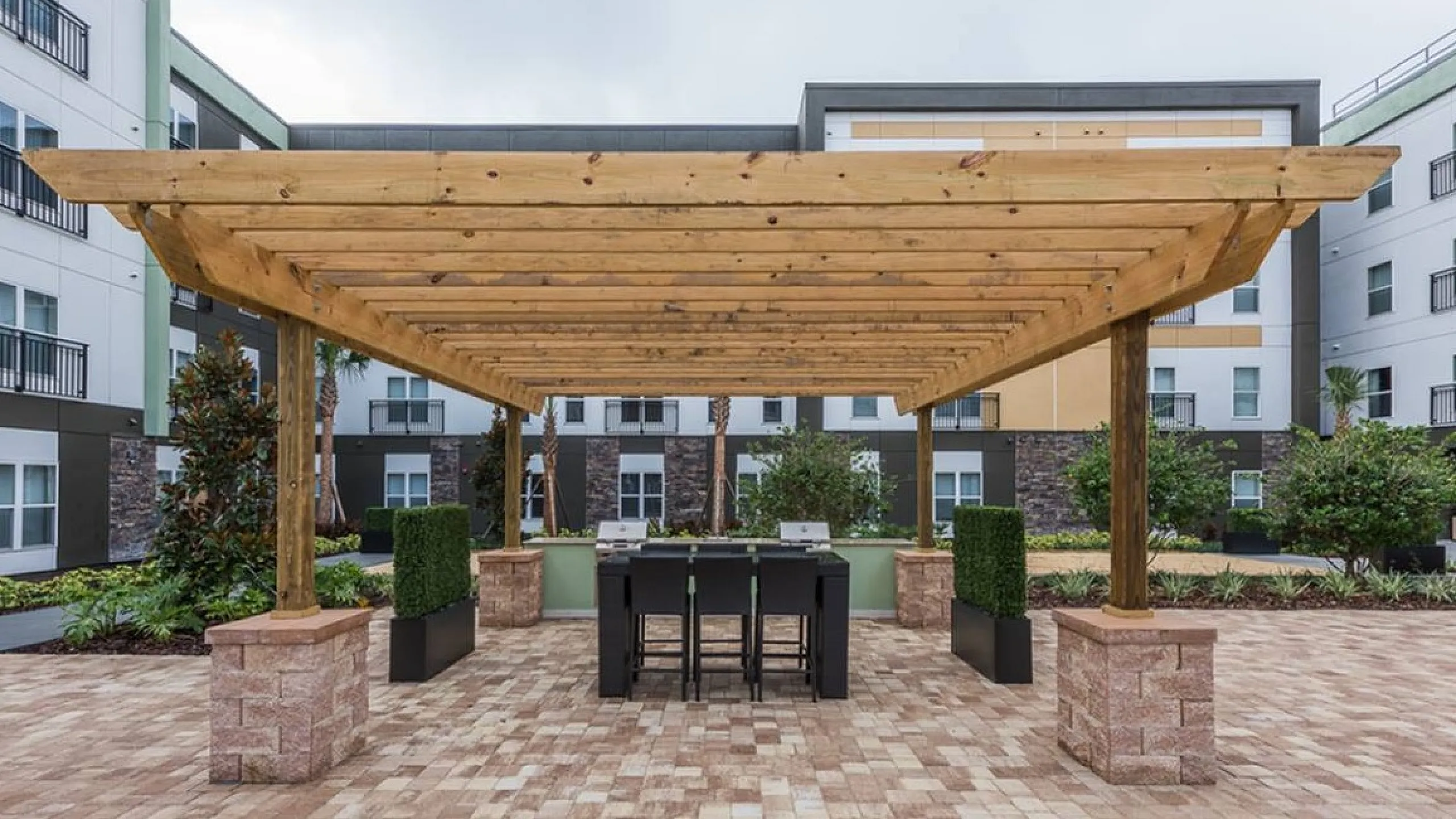 Inviting outdoor patio with a stylish wooden pergola, surrounded by lush landscaping, in a modern apartment complex.
