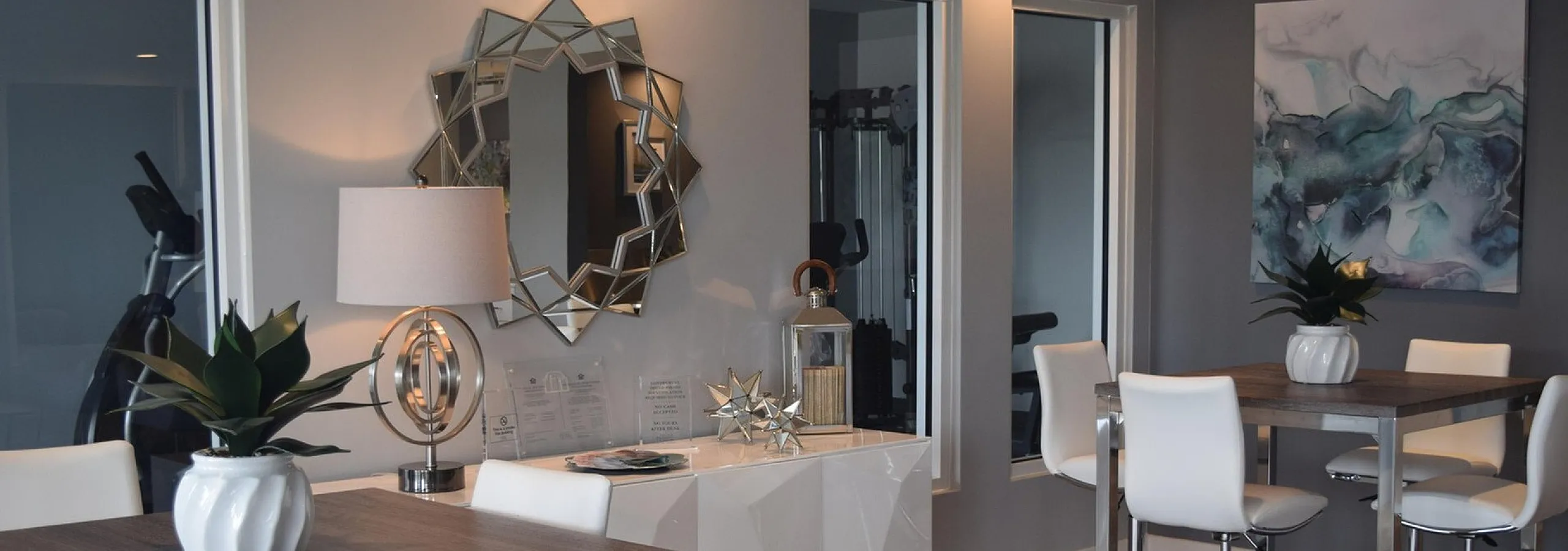 Modern dining area with elegant wooden tables, chic white chairs, and stylish decor including a geometric mirror and abstract artwork.