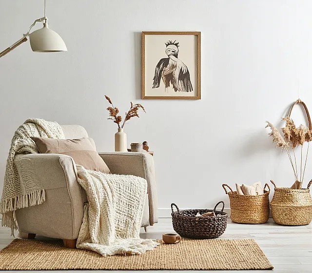 Cozy living space with a plush armchair draped in a soft knit throw, set against a minimalist backdrop adorned with tasteful wall art and decorative baskets.
