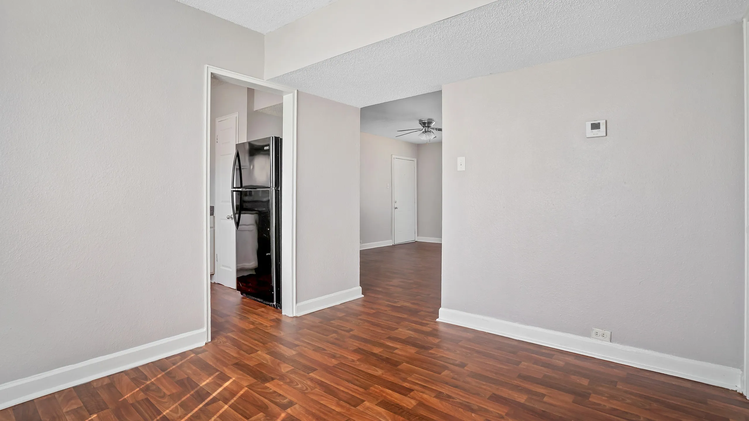 Bright apartment interior with elegant wooden flooring, open layout, and modern kitchen area featuring a sleek black refrigerator.