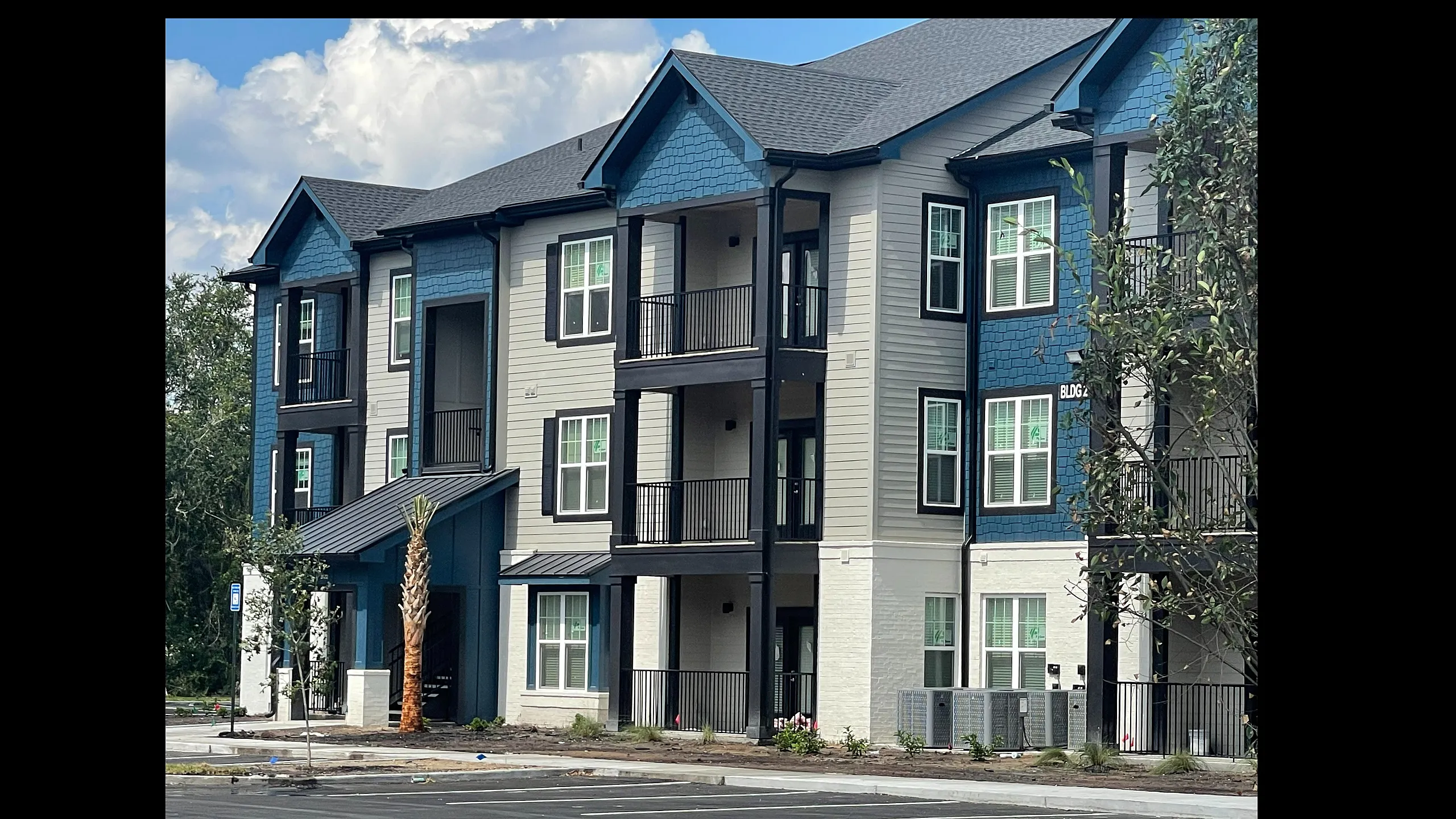 Modern apartment complex exterior with elegant balconies and stylish blue and white facade, surrounded by lush greenery.