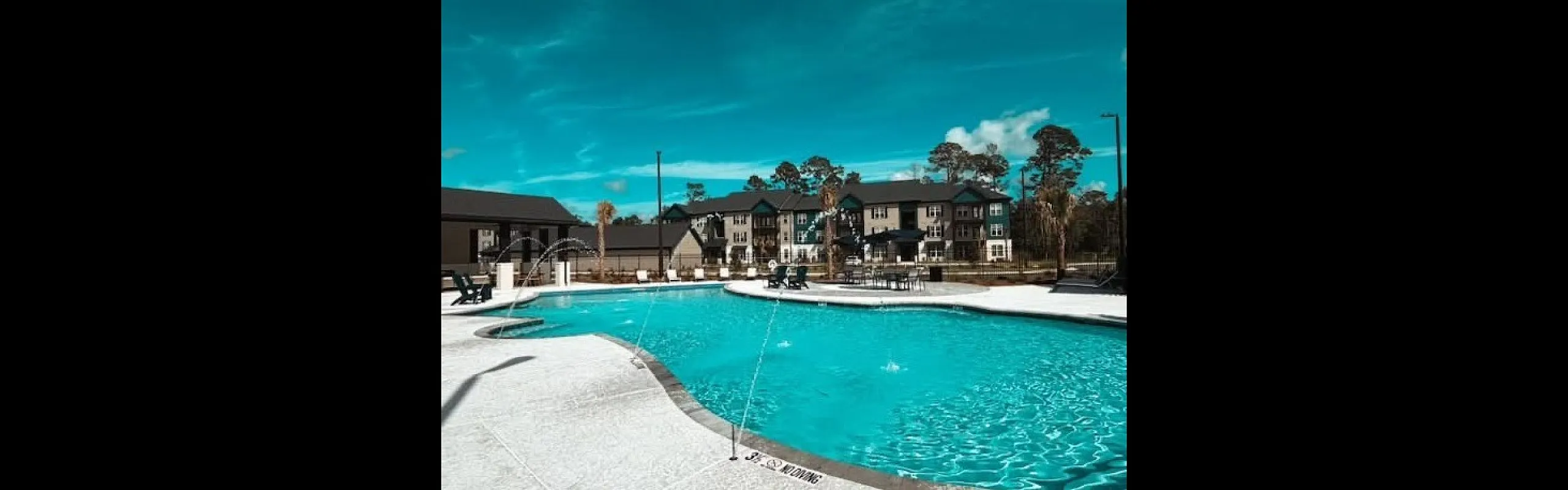 Luxurious apartment complex featuring a sparkling swimming pool with elegant lounge areas, surrounded by modern buildings and lush landscaping.
