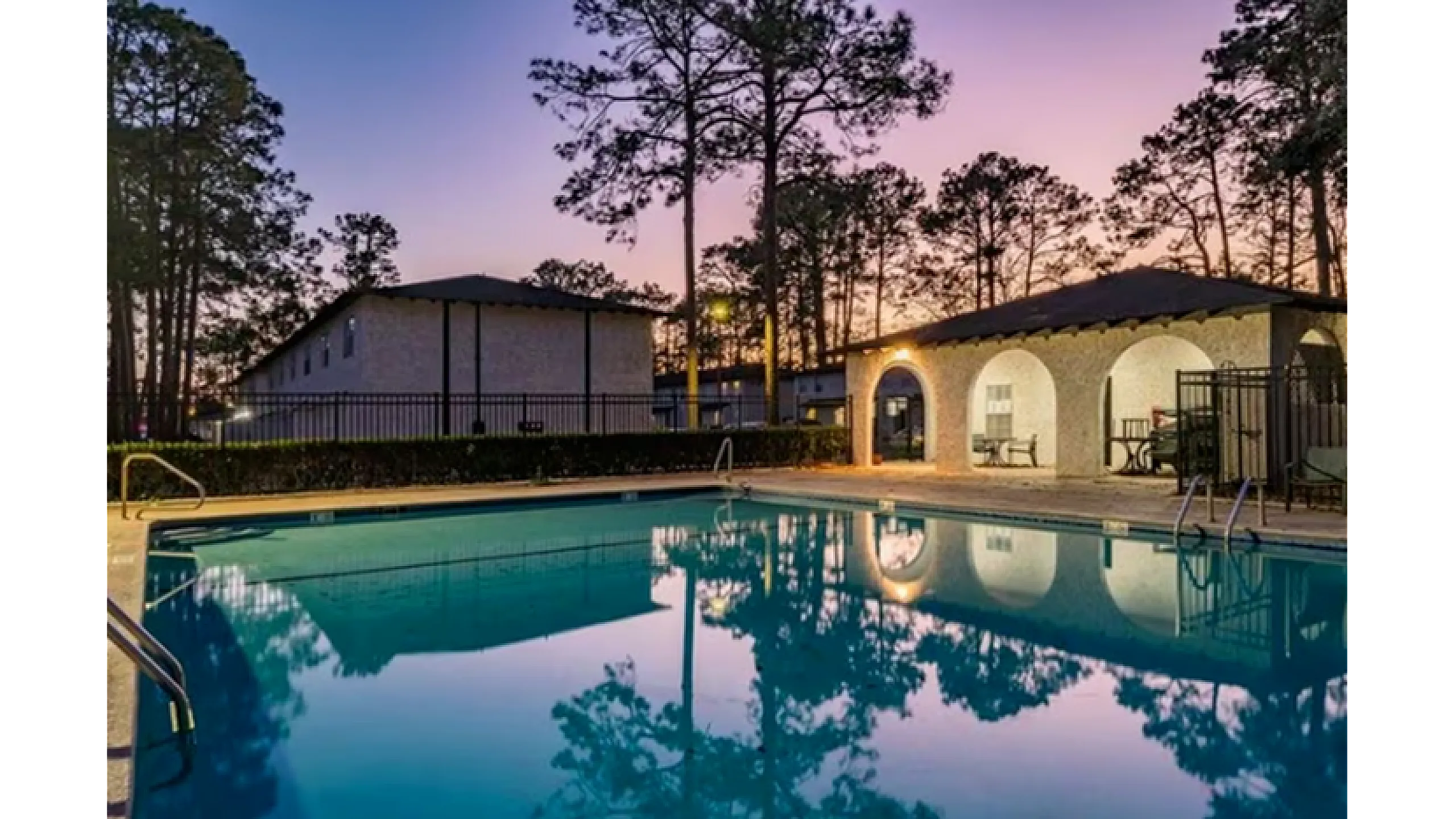 Elegant outdoor pool area at sunset with inviting warm lighting, surrounded by rustic architecture and lush pine trees.