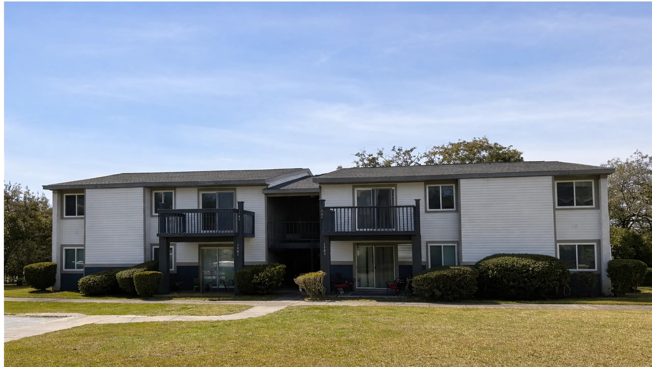 Charming two-story apartment building with private balconies, surrounded by lush greenery and well-maintained lawns.
