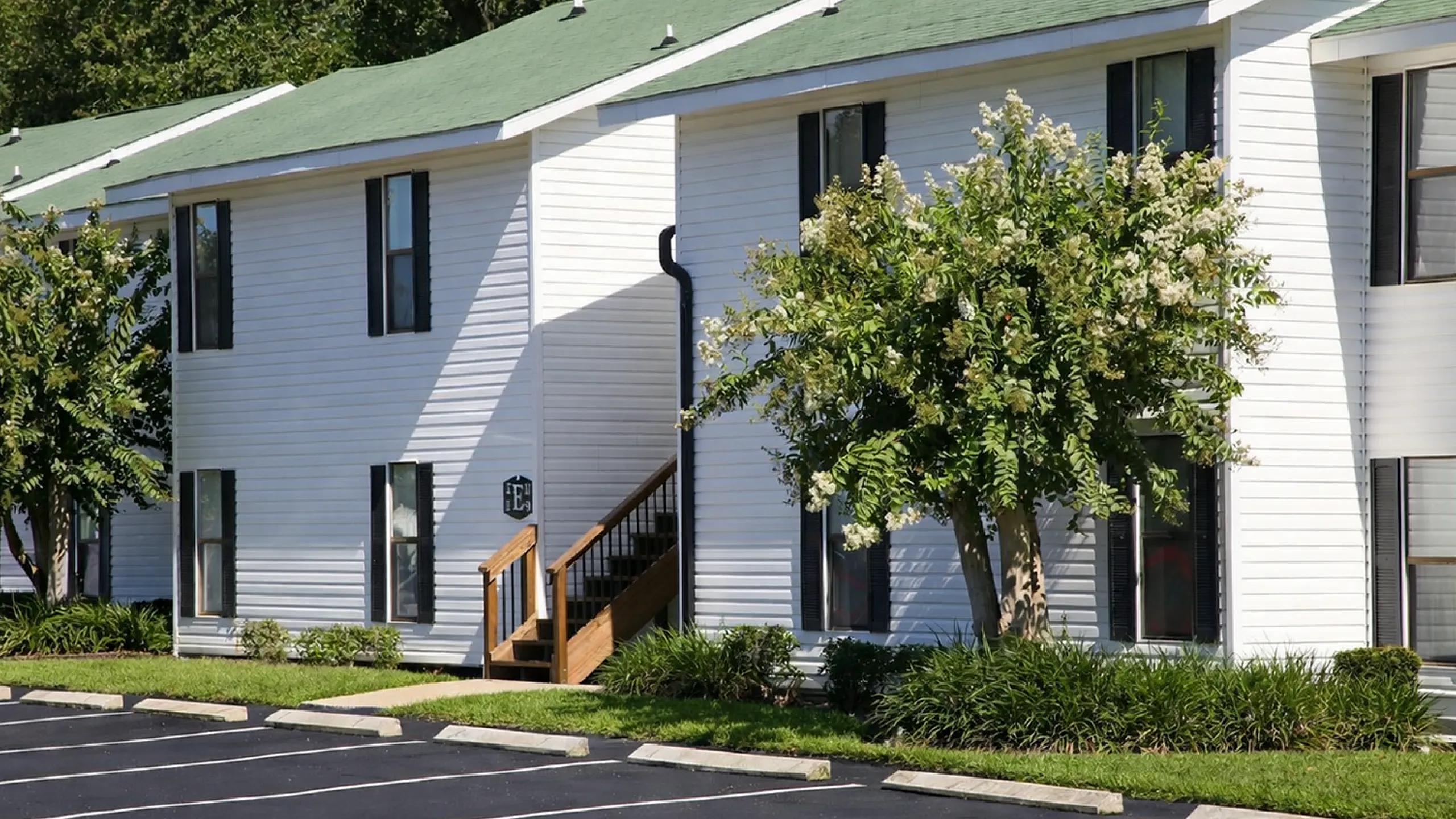 Charming white apartment building with green roofs, surrounded by lush greenery and ample parking space.