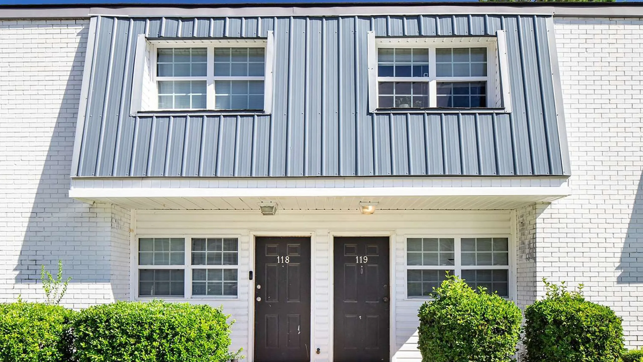 Charming duplex with modern exterior featuring sleek metal roofing and well-maintained shrubbery, perfect for stylish urban living.