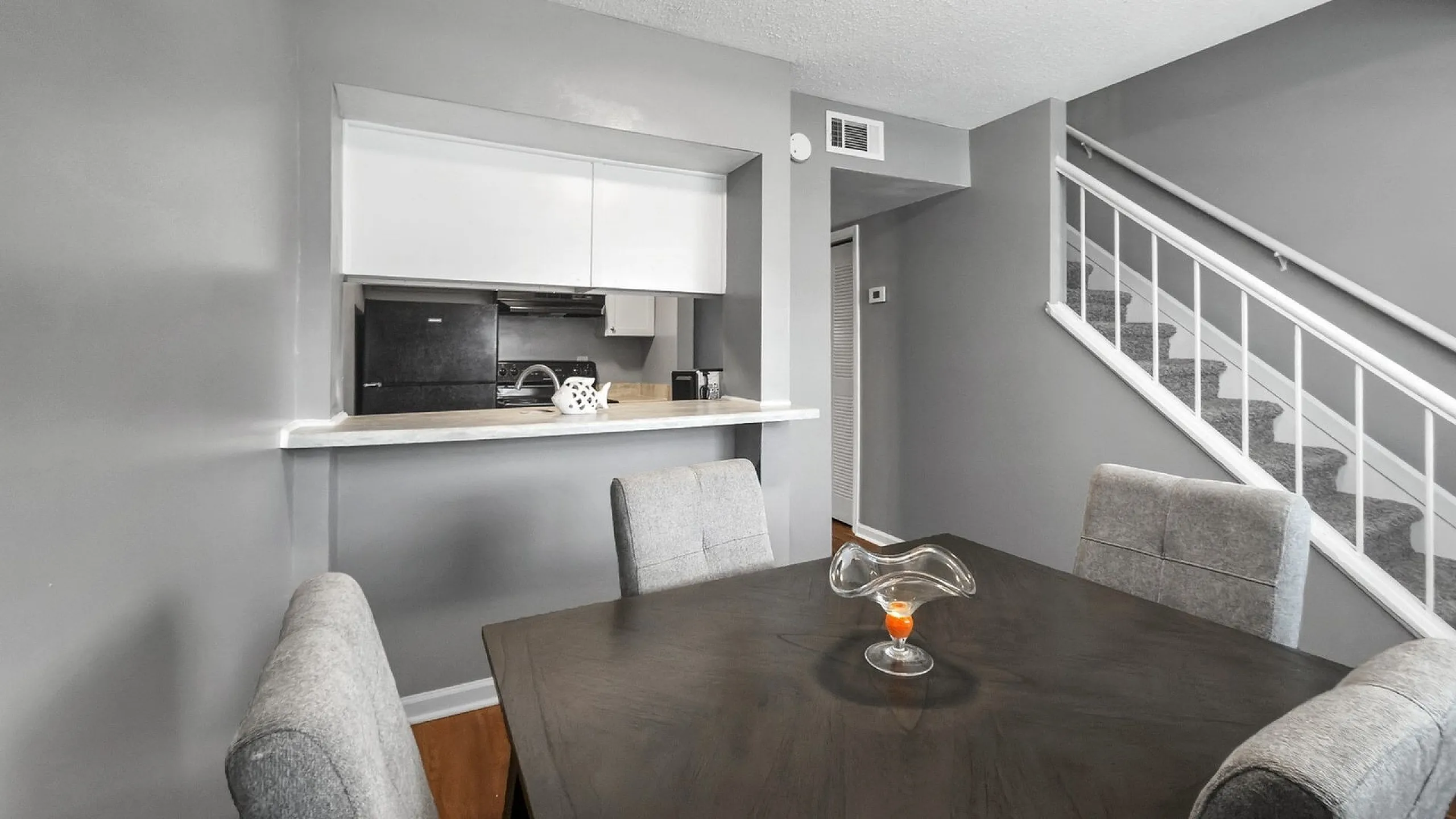 Modern dining area with elegant gray seating, adjacent to an open kitchen pass-through, complemented by a stylish staircase in a contemporary apartment.