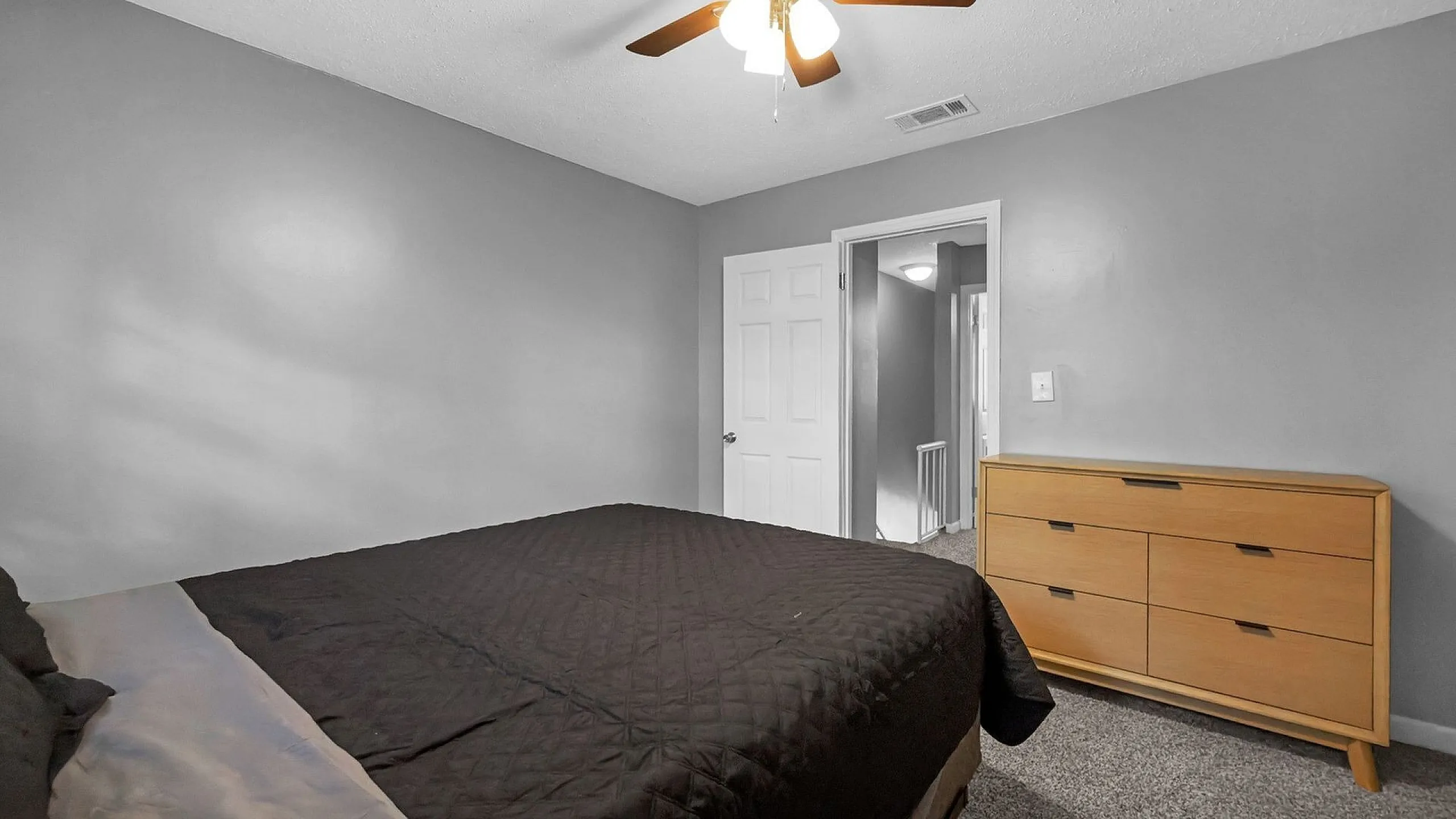 Inviting bedroom with neutral tones, cozy carpet, stylish dresser, and a modern ceiling fan.