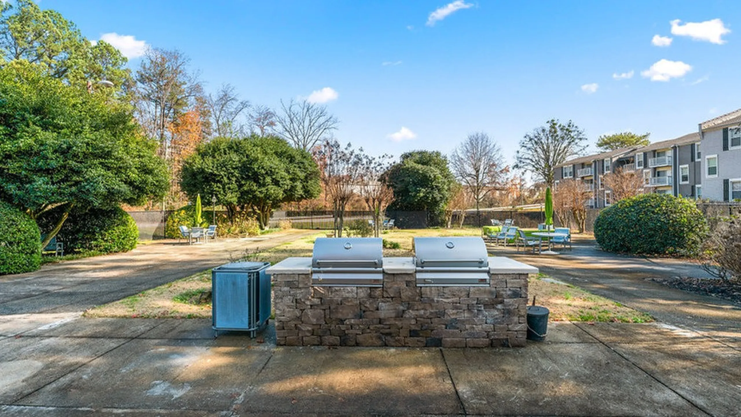 Elegant outdoor area with dual grills set against lush greenery and modern apartment buildings, perfect for social gatherings.
