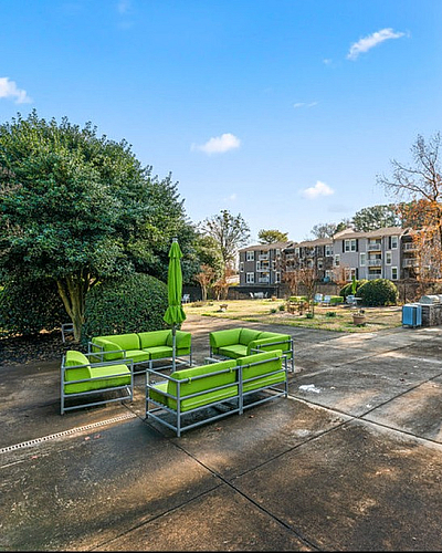 Inviting outdoor patio with modern green seating set amidst lush greenery and apartment views.