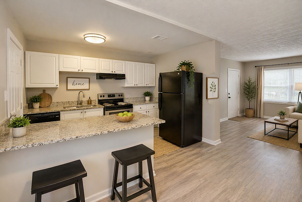 Inviting open-concept kitchen and living room with modern design, featuring sleek black appliances, light granite countertops, and stylish decor.