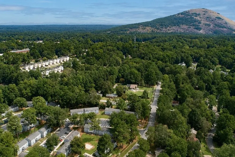 Aerial view of a peaceful residential community surrounded by lush greenery, with scenic mountain views in the background.