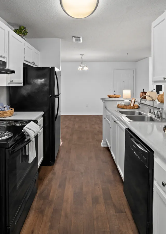 Modern kitchen with sleek black appliances, white cabinetry, and elegant wood flooring, offering a stylish and functional space.