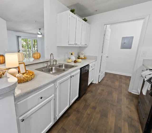 Bright and inviting kitchen with modern white cabinetry, sleek countertops, and warm wooden floors, leading into a sunlit living space.