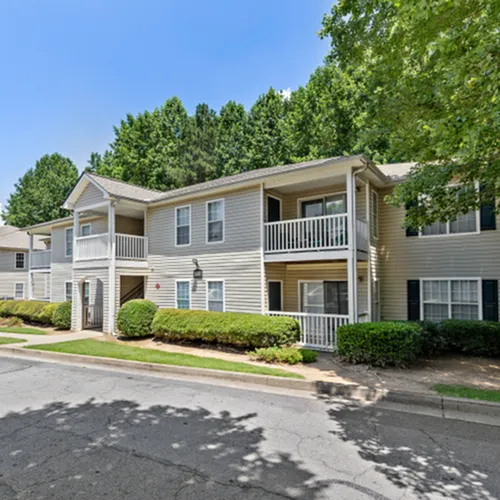 Charming apartment building with two levels, featuring white siding, spacious balconies, and surrounded by lush greenery in a tranquil setting.