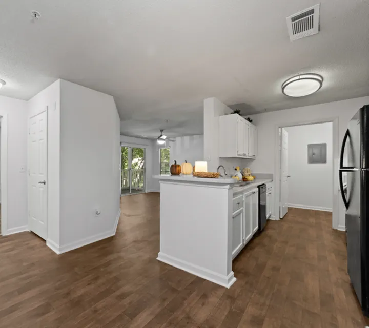 Bright and modern kitchen with sleek white cabinetry, open layout leading to a cozy living area with natural light and balcony access. Elegant hardwood floors throughout.