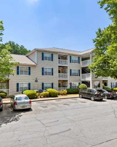 Charming three-story apartment building with balconies, nestled among lush greenery and ample parking space.