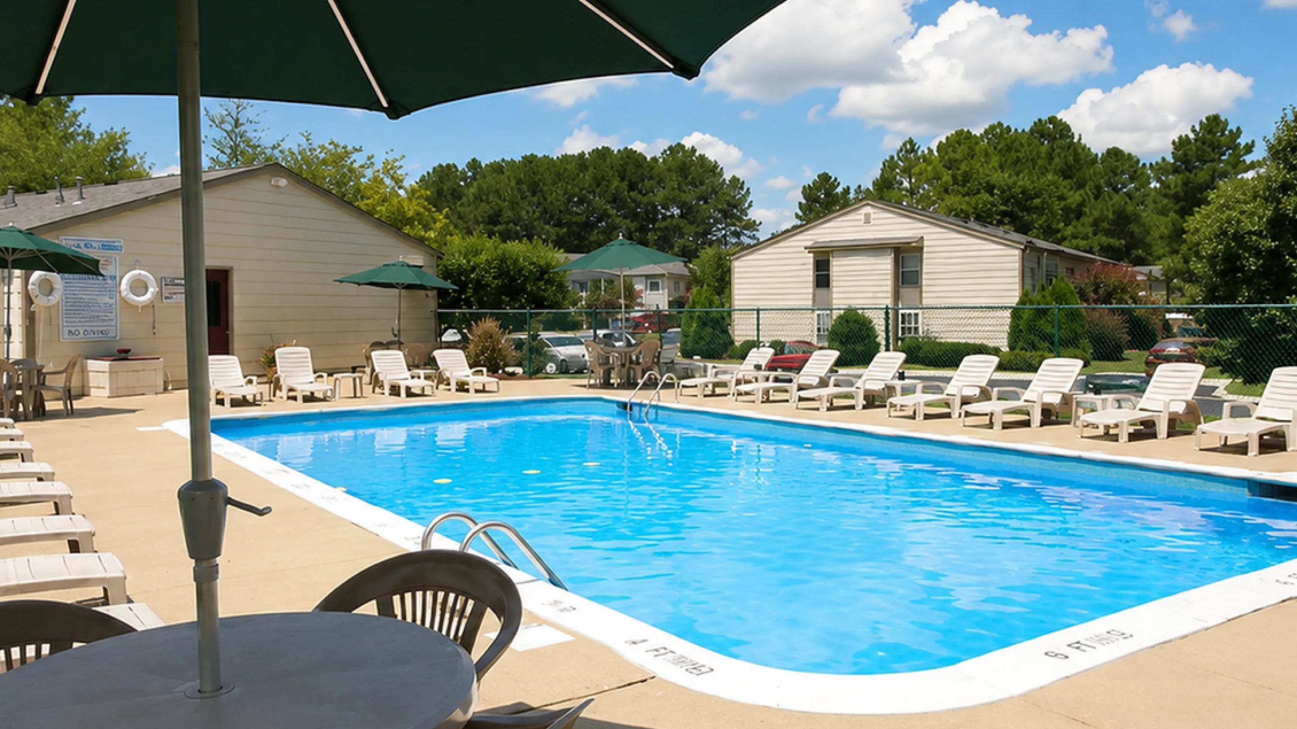 Inviting community swimming pool with sun loungers and shaded seating, surrounded by lush greenery and bright blue skies.