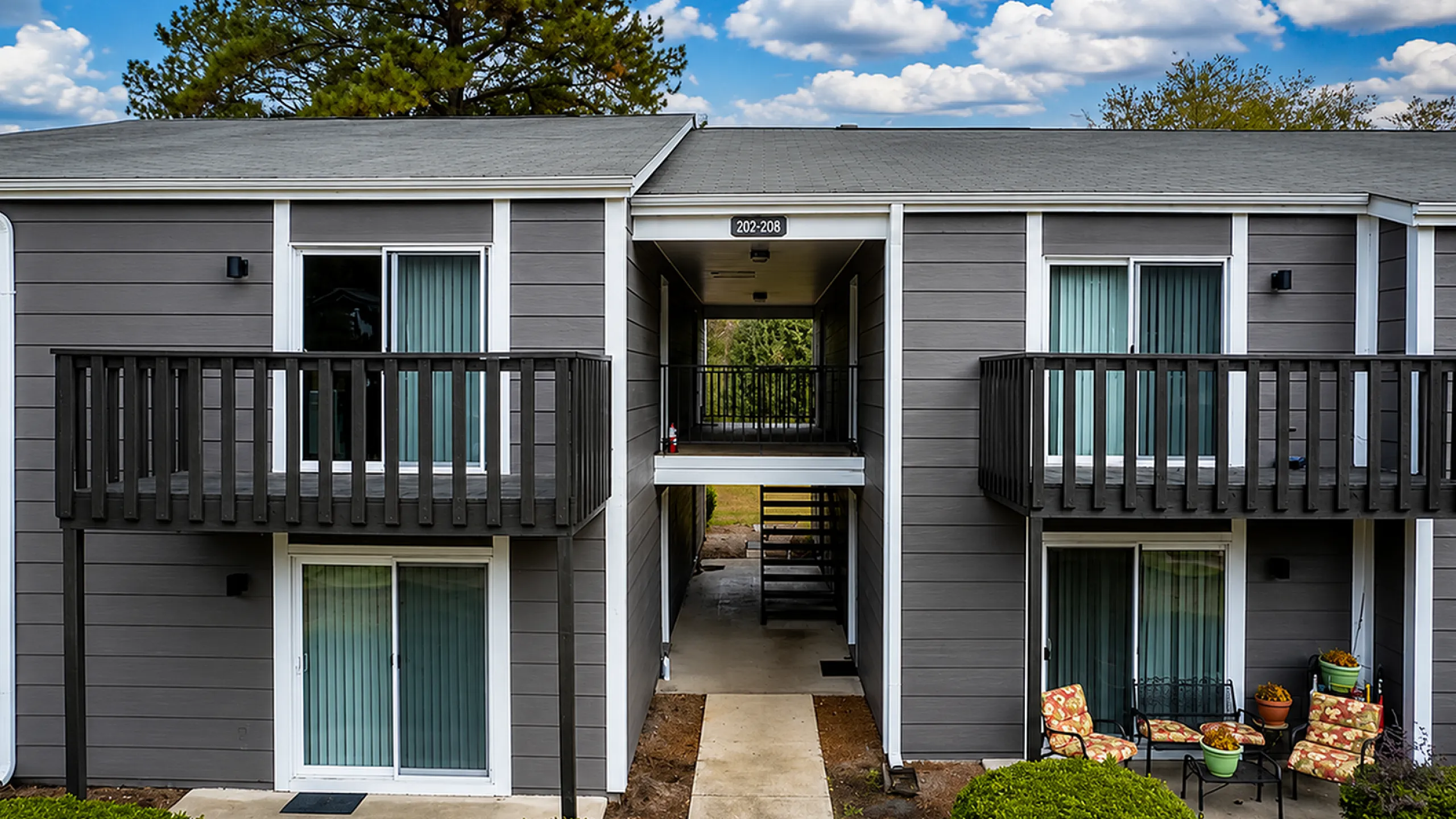 Charming two-story apartment building with private balconies, surrounded by lush greenery and vibrant outdoor seating.