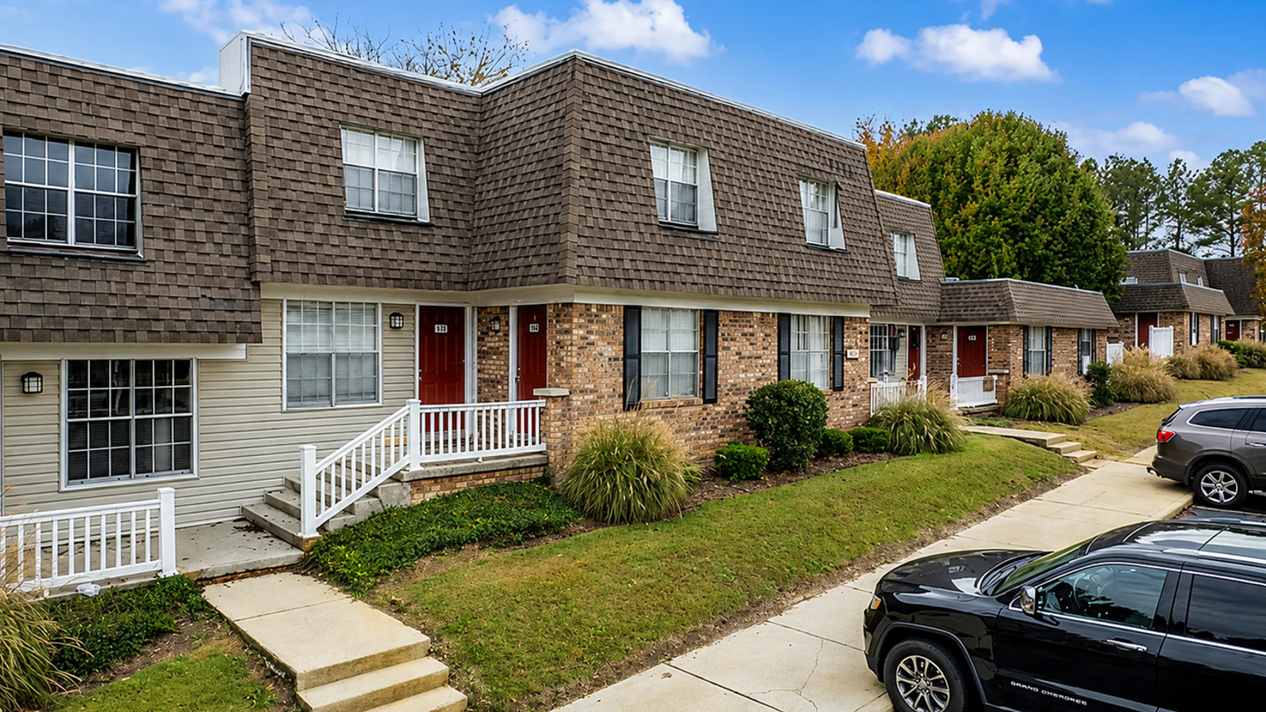 Charming townhouse row with brick facade, featuring inviting front porches and manicured landscaping under a bright blue sky.