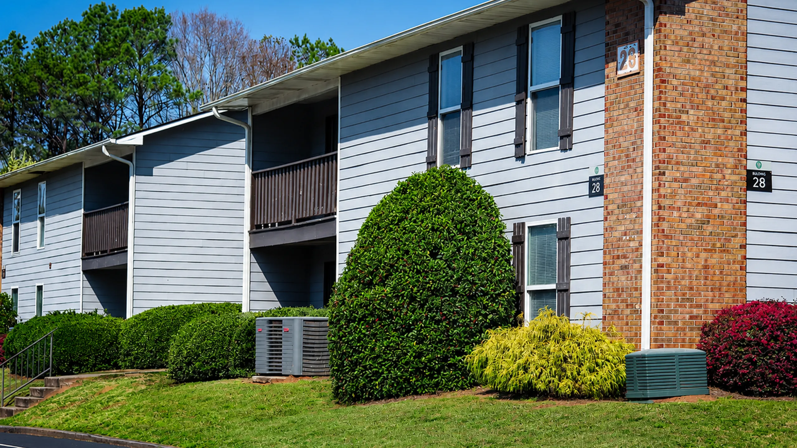 Charming apartment building with modern gray siding, complemented by lush greenery and neatly trimmed bushes, offering a serene living environment.