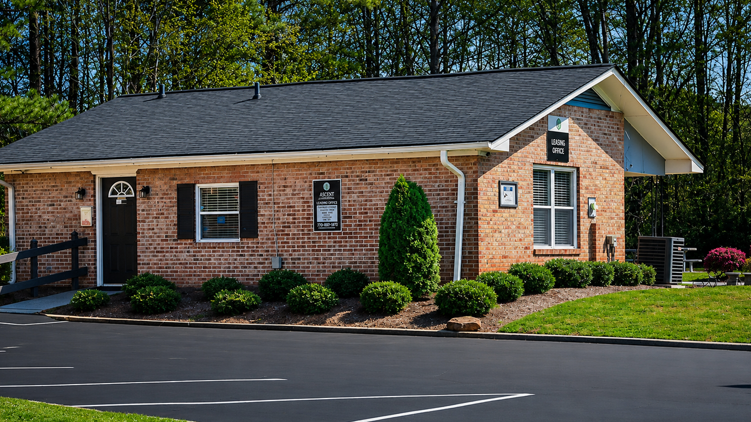 Charming brick leasing office surrounded by lush greenery and well-maintained landscaping.