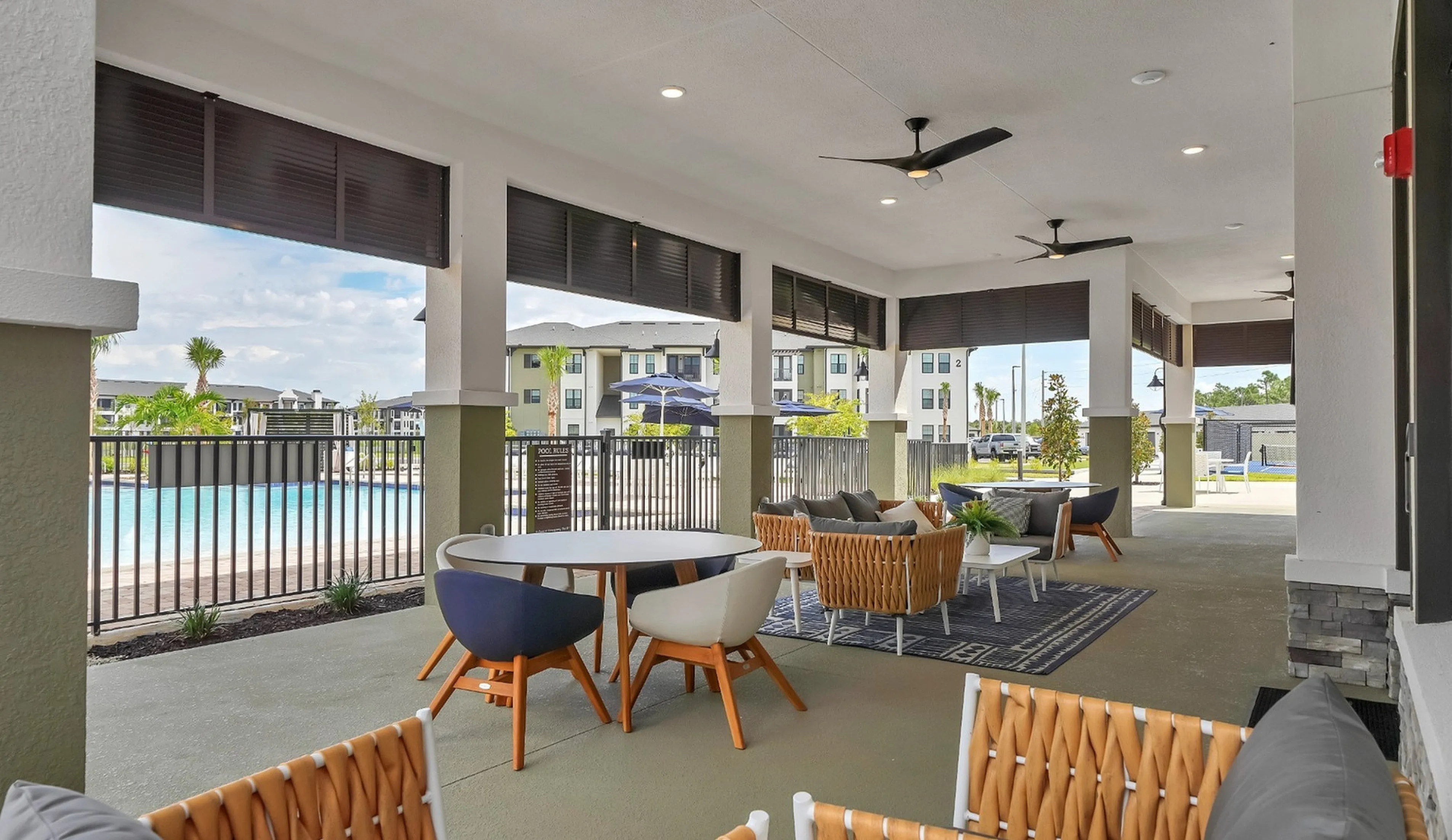 Modern covered patio overlooking beautiful pool area, featuring stylish outdoor seating and ceiling fans for ultimate relaxation.