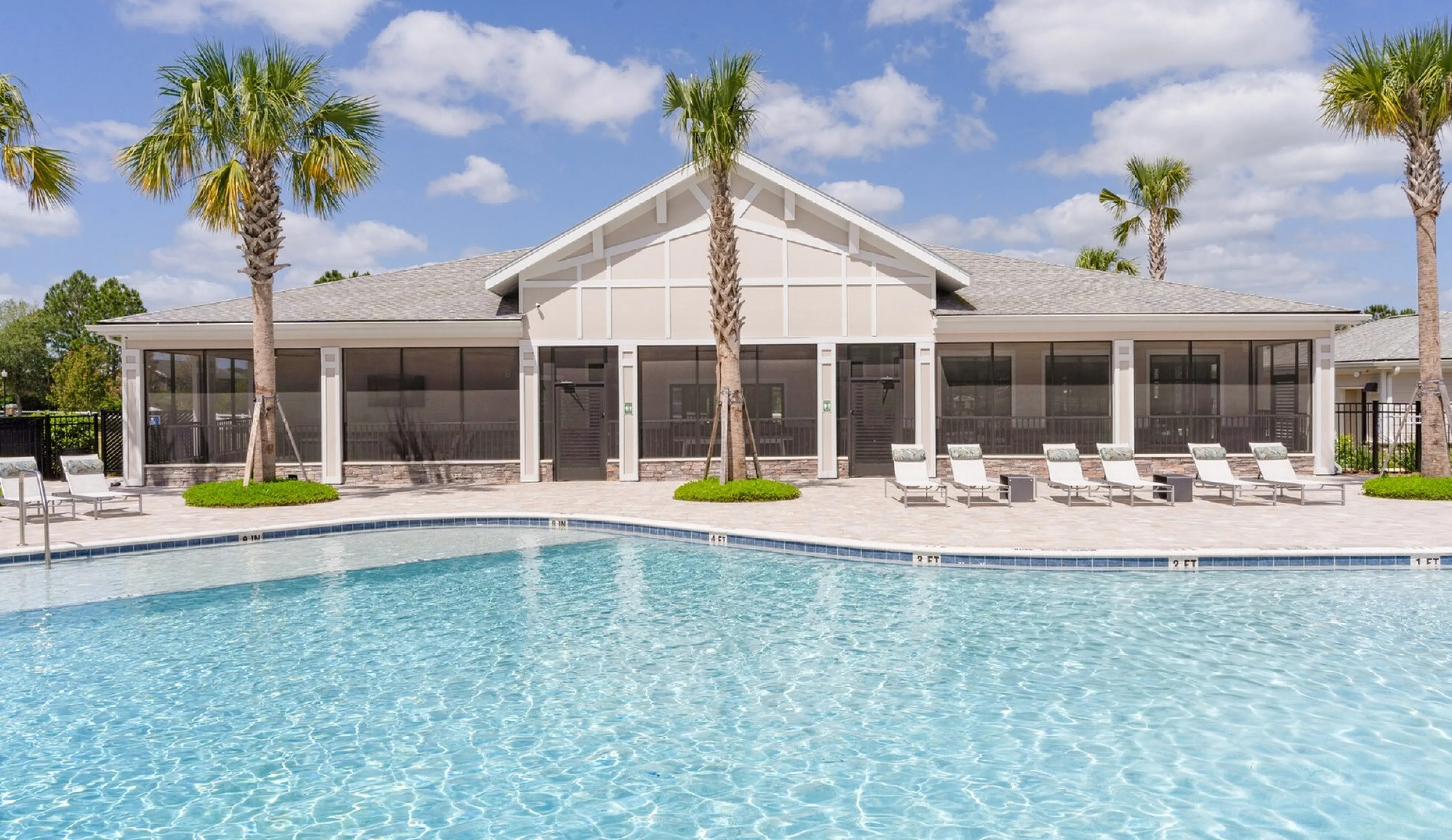 Luxurious apartment pool area with sparkling blue water, surrounded by elegant palm trees and modern sun loungers under a clear sky.