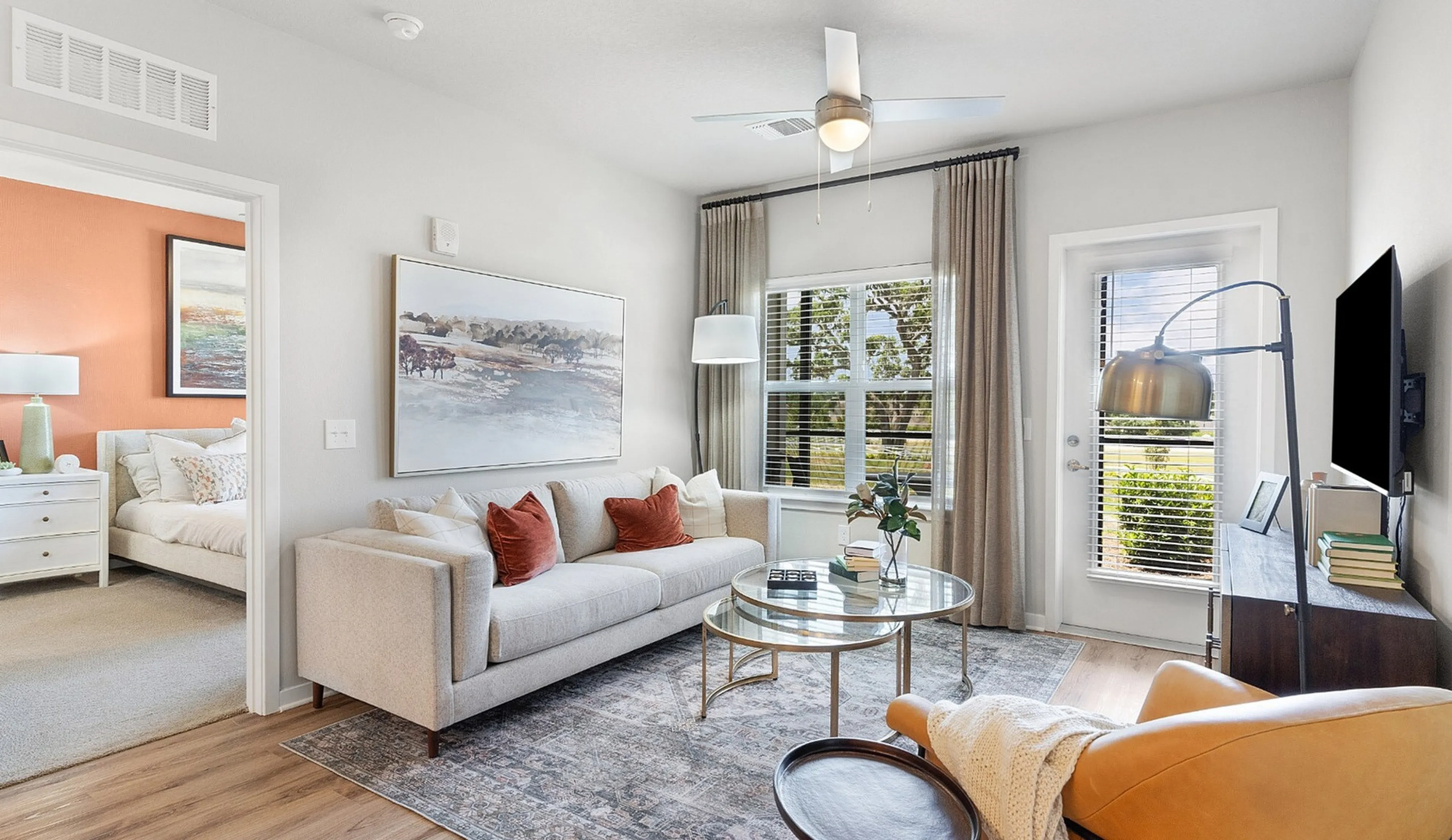 Bright and inviting living room with stylish furnishings, featuring a cozy beige sofa, modern round coffee table, and vibrant accent pillows. Large windows offer ample natural light.
