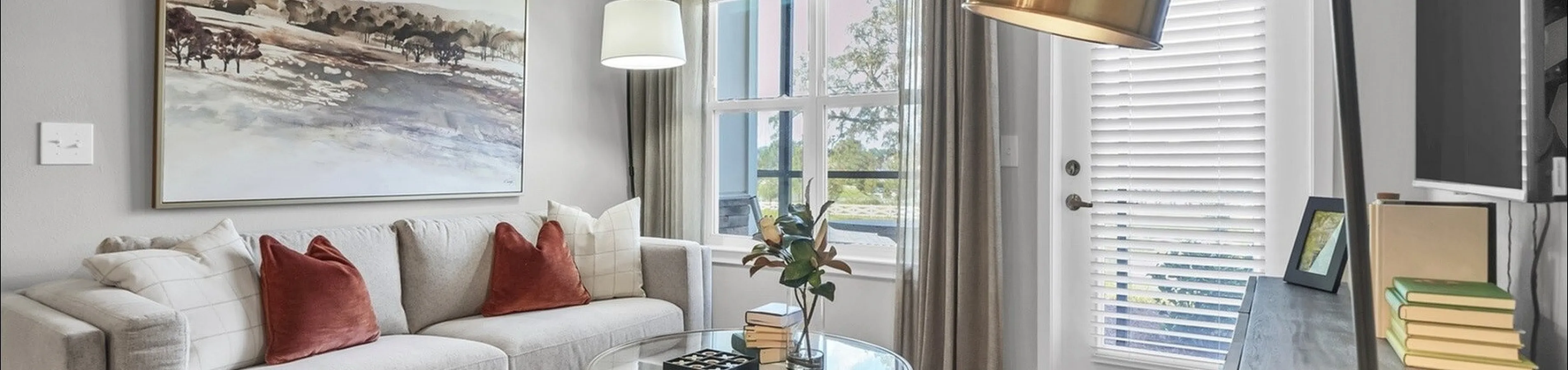 Bright and welcoming living room showcasing modern decor with a comfortable sofa, elegant lighting, and a stylish glass coffee table. Large windows adorned with flowing curtains enhance the inviting atmosphere.