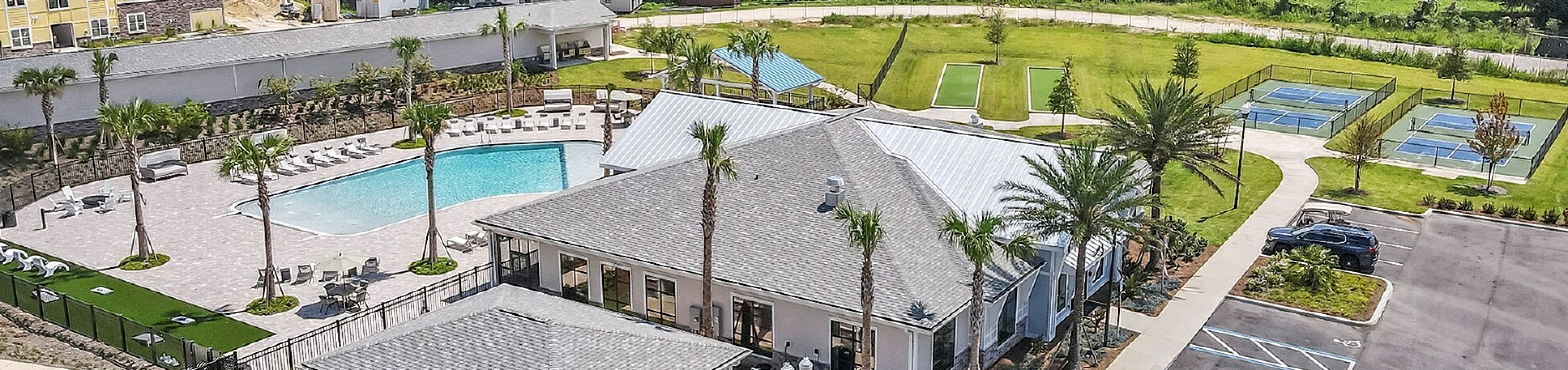 Luxurious apartment complex featuring a sparkling pool, landscaped gardens, tennis courts, and ample parking, set against a lush green backdrop.
