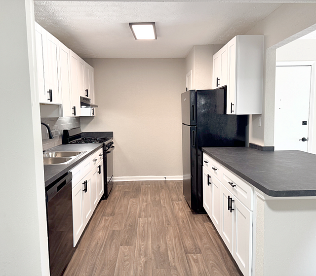 Chic modern kitchen with sleek black appliances, elegant white cabinetry, and warm wood-style flooring.