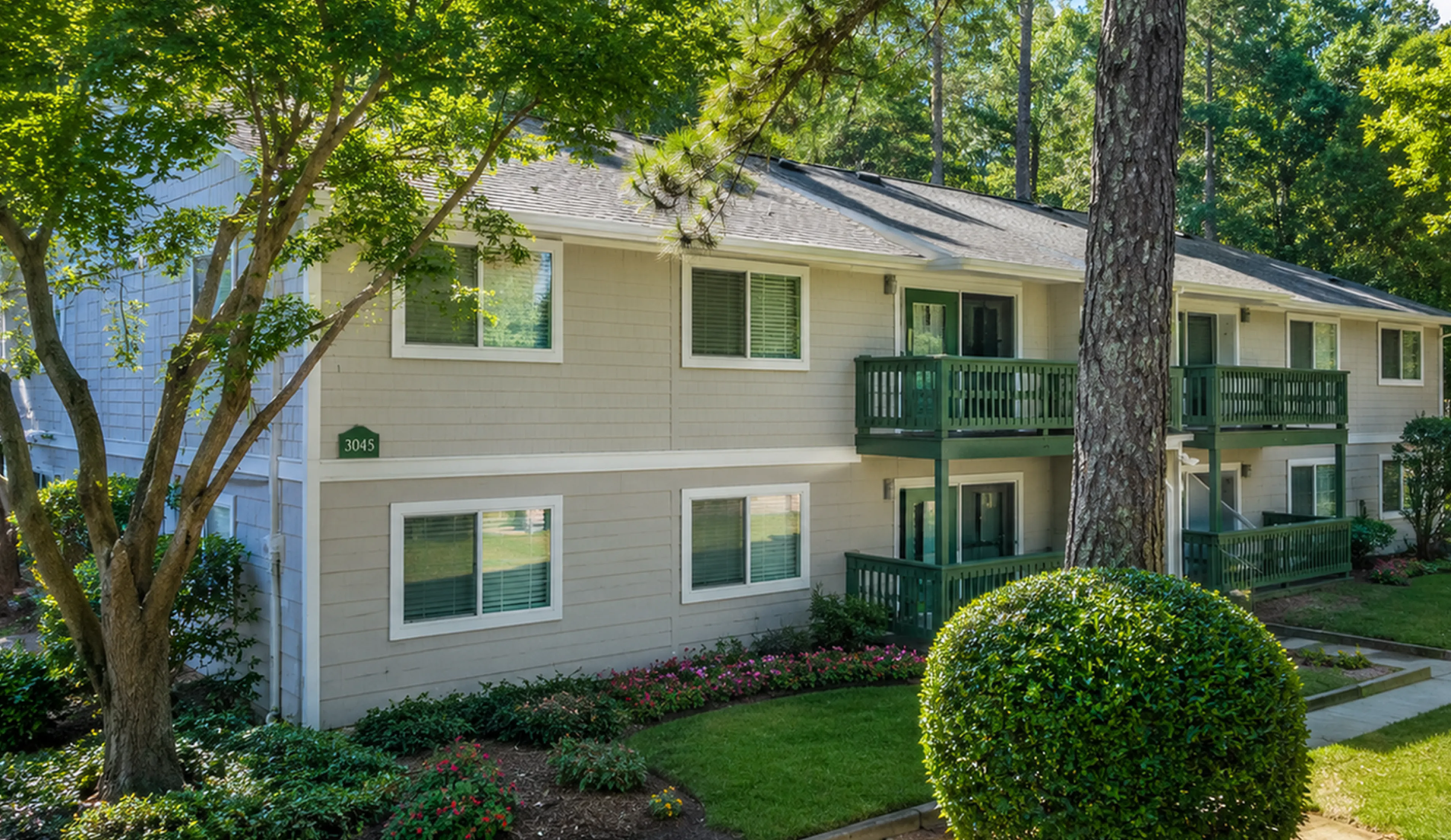 Charming two-story apartment building with modern balconies, surrounded by lush greenery and vibrant landscaping.