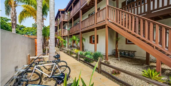 Charming apartment exterior with wooden staircases and lush palm trees, offering a welcoming atmosphere.