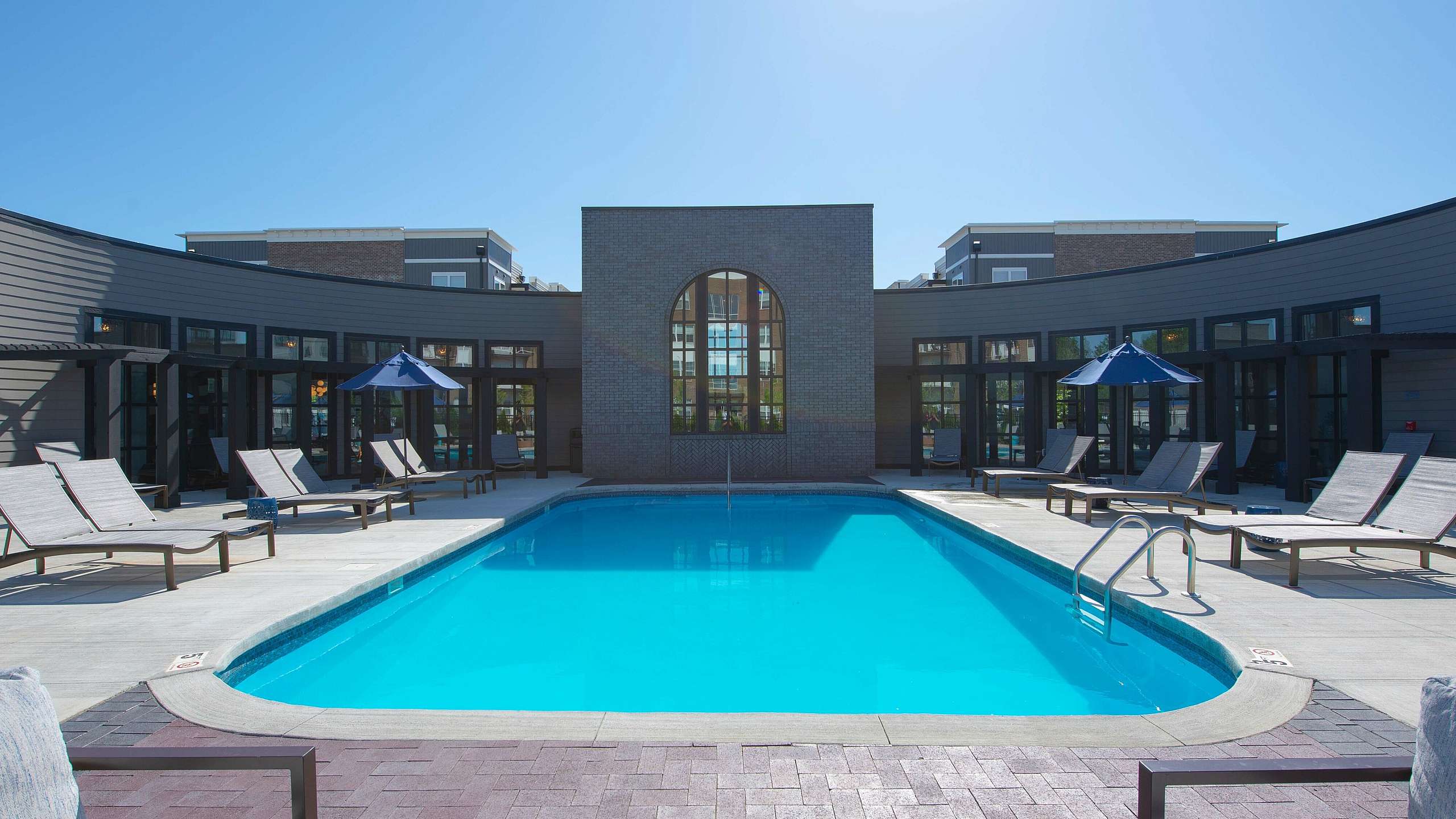 Luxurious apartment complex pool area featuring a sun-drenched, crystal-clear swimming pool surrounded by elegant loungers and modern design.
