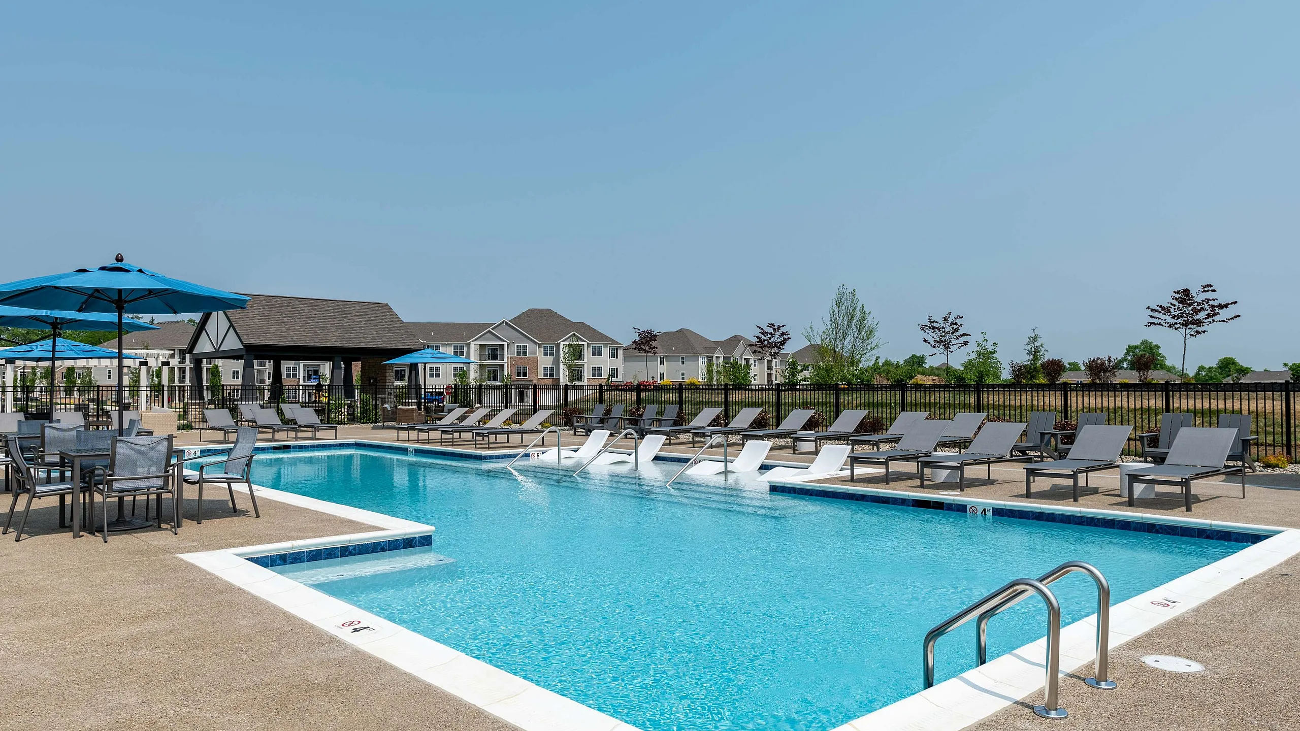 Inviting outdoor pool area with sleek loungers and umbrellas, surrounded by modern residential buildings, perfect for relaxation and leisure.