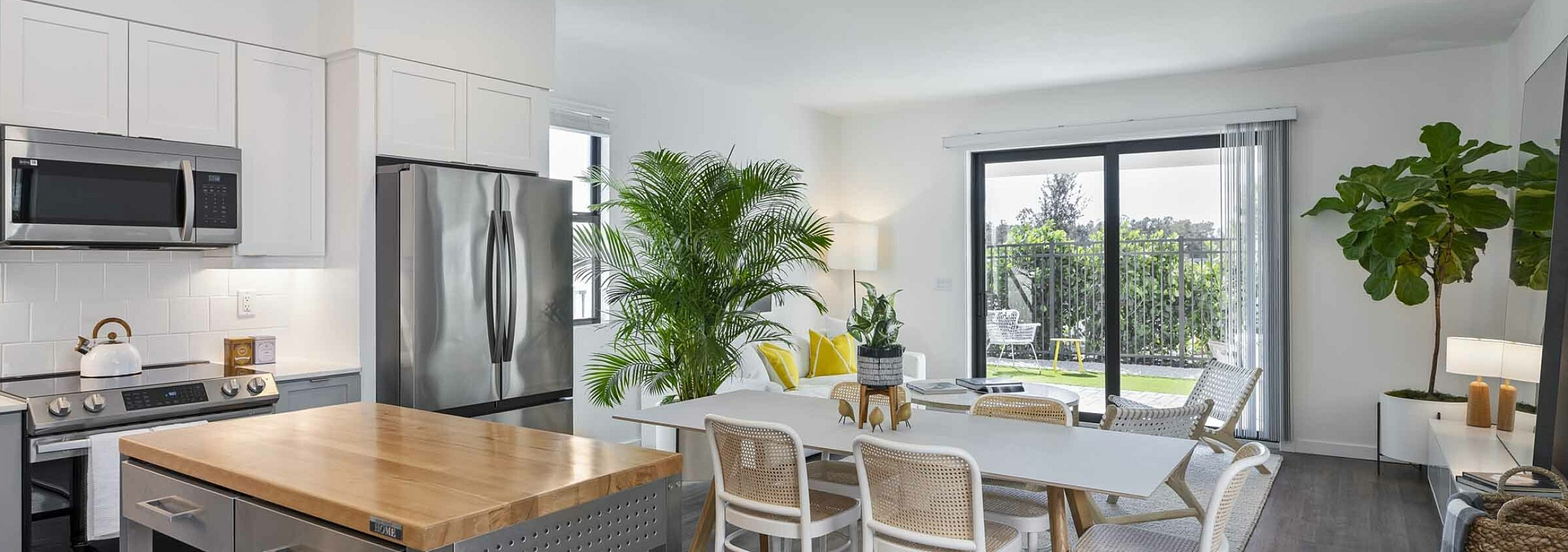 Modern open-concept kitchen and dining area with sleek appliances and abundant natural light, enhanced by lush indoor plants and a view of a serene patio.