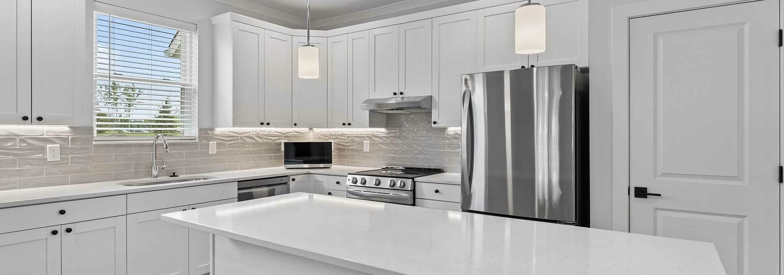 Modern kitchen with sleek white cabinets, stainless steel appliances, and elegant pendant lighting over a spacious island.